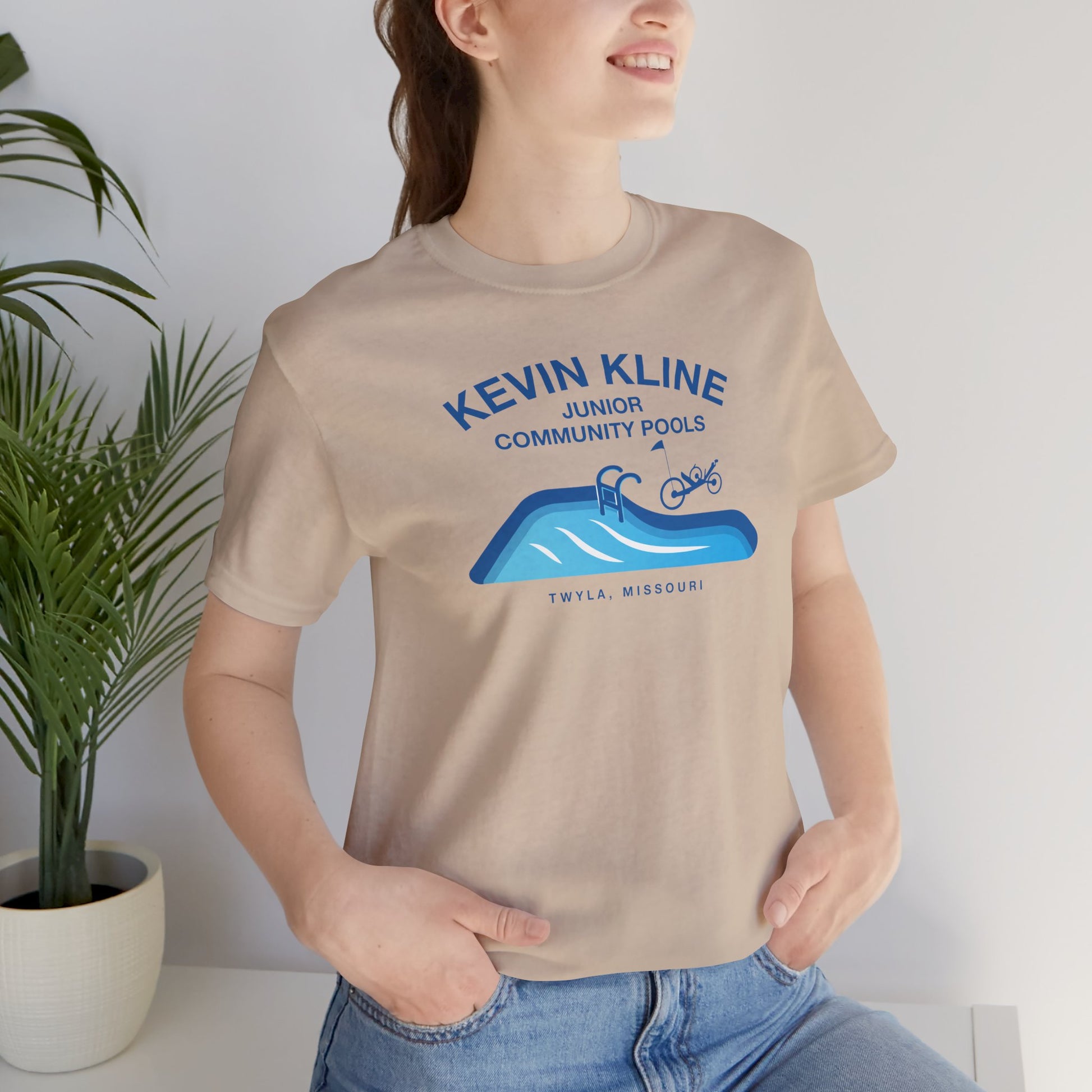 Woman wearing tan DTF St. Louis Kevin Kline Junior Community Pools graphic tee with pool and recumbent trike.