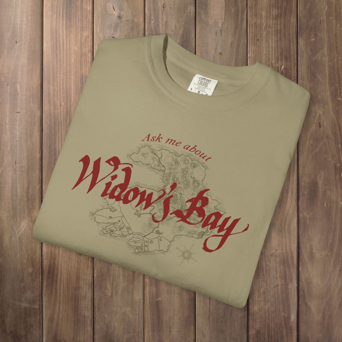 Folded khaki Comfort Colors tee with a vintage island map and antique "Ask Me About Widow's Bay" type from the Apple TV show