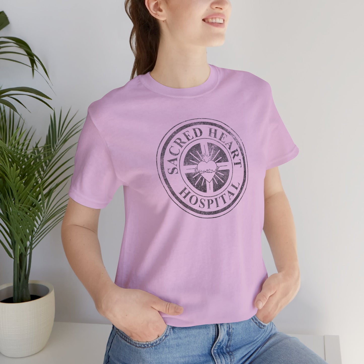 Woman wearing lilac Bella Canvas 3001 tee with vintage distressed Sacred Heart Hospital logo from Scrubs printed on chest.