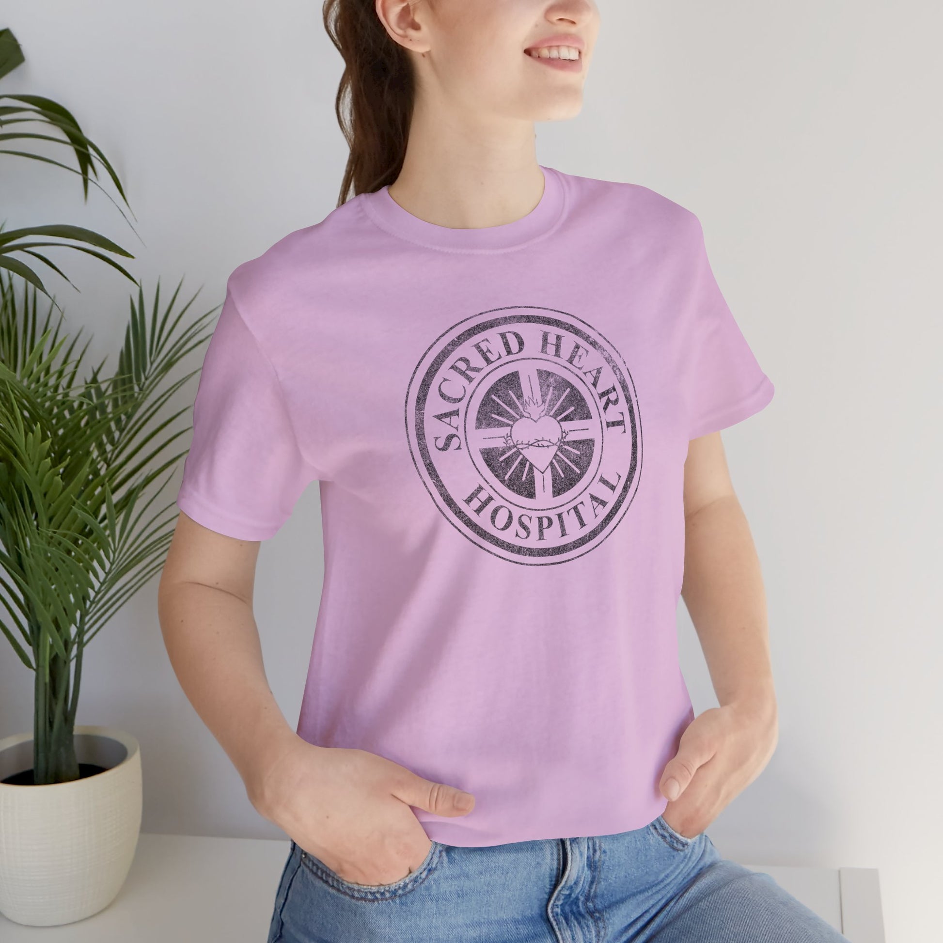 Woman wearing lilac Bella Canvas 3001 tee with vintage distressed Sacred Heart Hospital logo from Scrubs printed on chest.