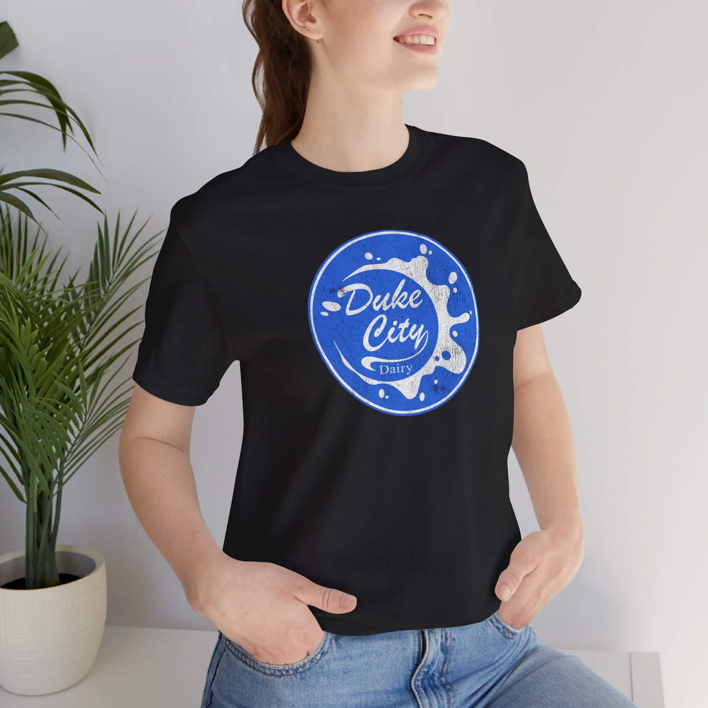 Woman wearing black t-shirt with vintage distressed Duke City Dairy logo inspired by TV Show Pluribus.