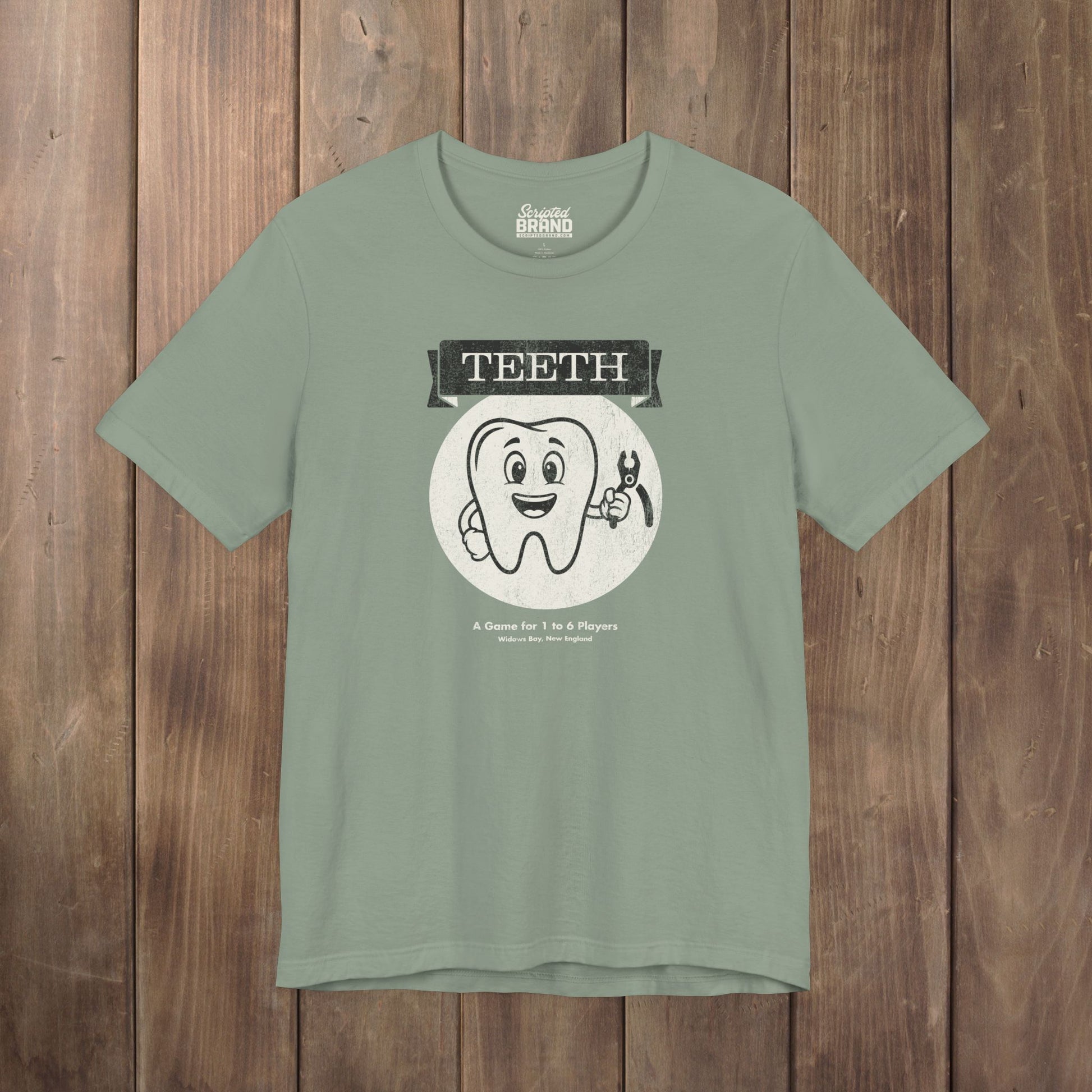 Sage green Bella+Canvas tee with the vintage TEETH board game box cover from Widow's Bay, a smiling tooth holding pliers