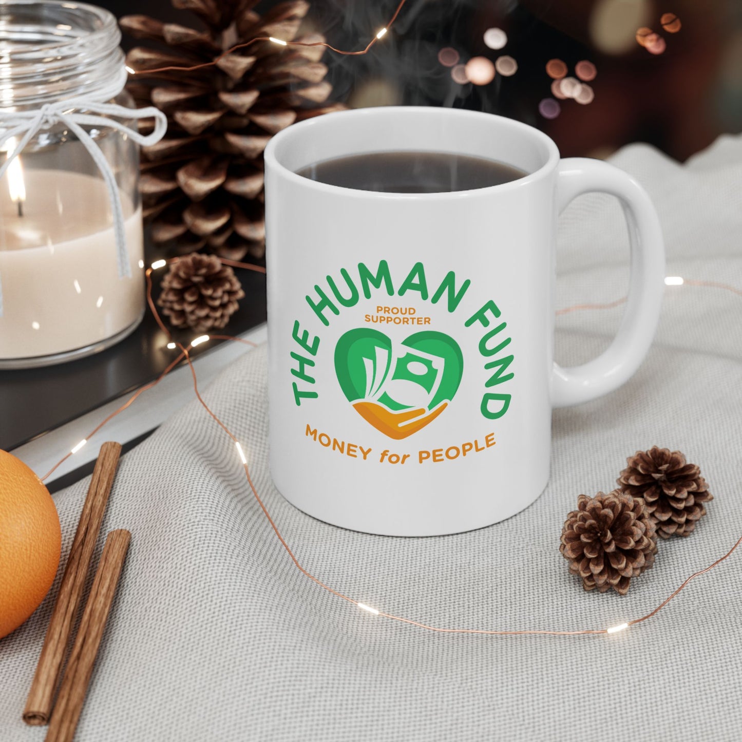 White mug with 'The Human Fund' logo on a table with decorative items