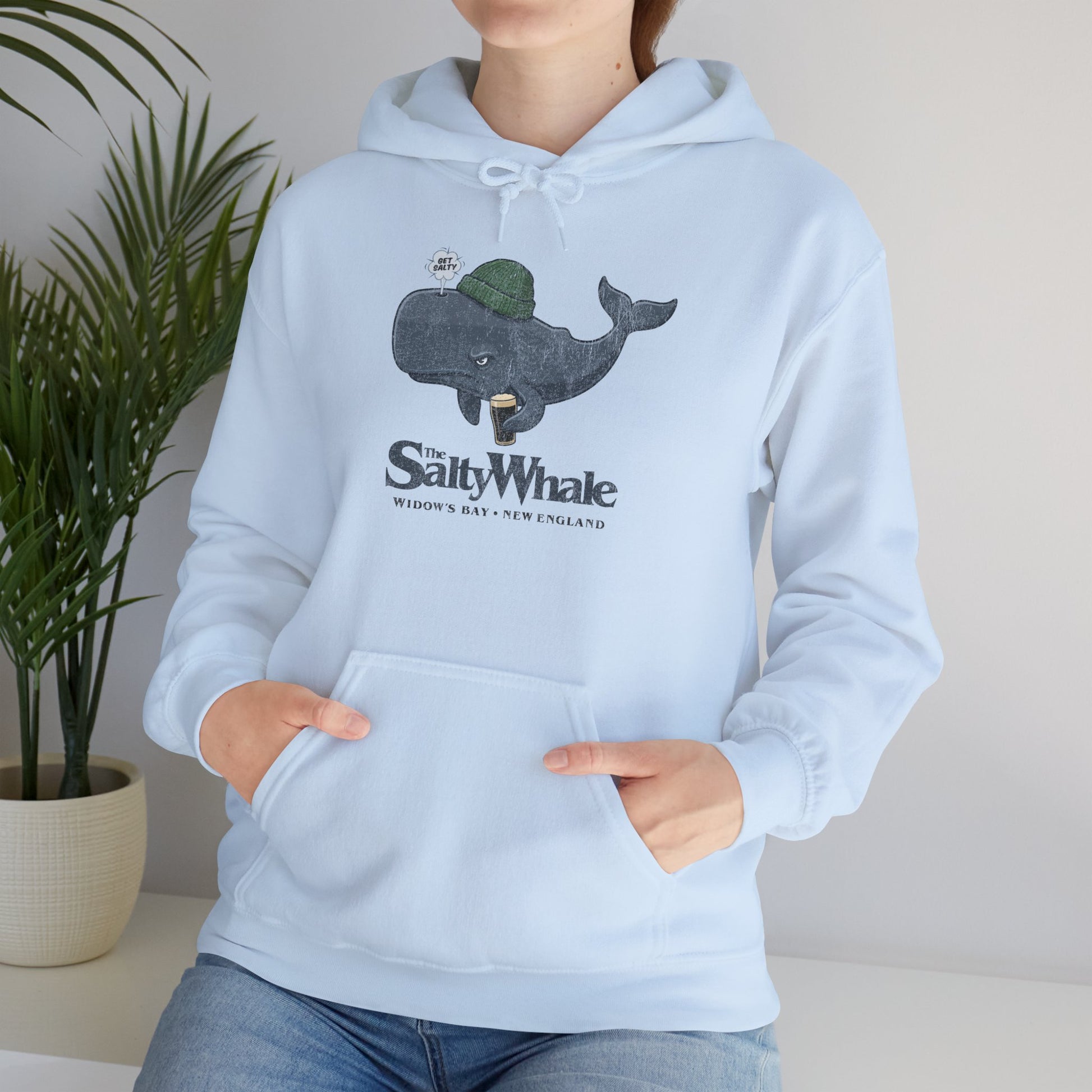 Woman wearing light blue 'The Salty Whale' cartoon mascot hoodie inspired by Widow's Bay Apple TV series, heavy blend pullover sweatshirt