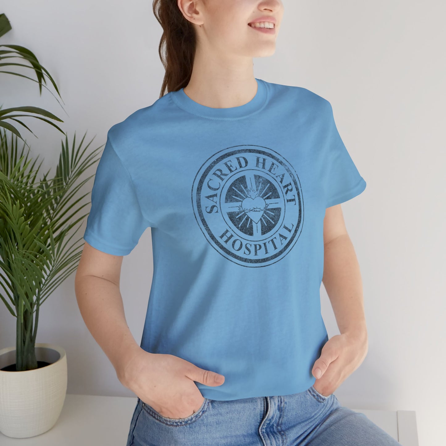 Woman wearing Ocean blue Bella Canvas 3001 tee with vintage distressed Sacred Heart Hospital logo from Scrubs printed on chest.