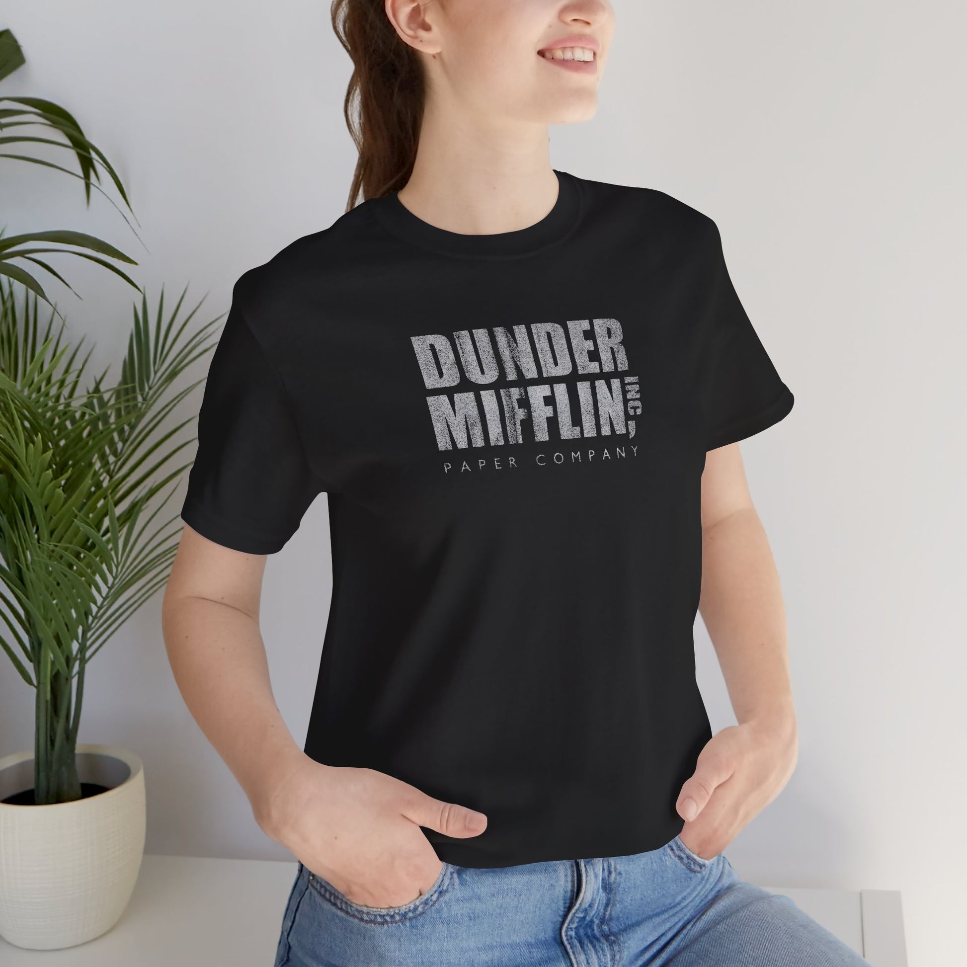 Woman wearing a black t-shirt featuring the Dunder Mifflin logo from the TV show The Office in a vintage distressed style.