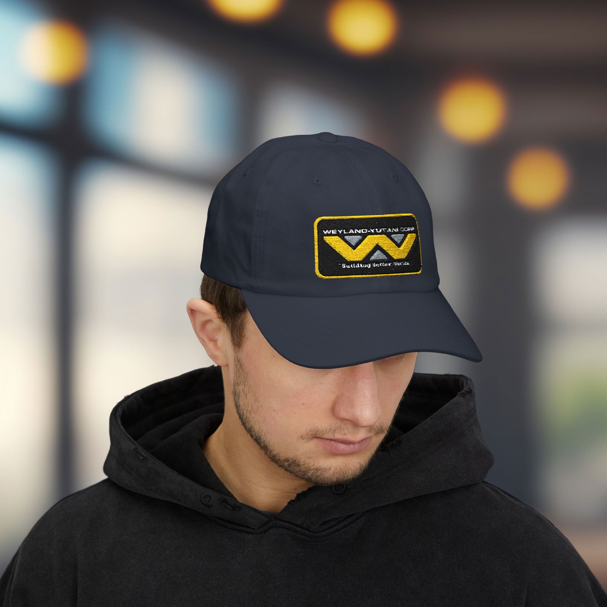 Man wearing navy blue Yupoong dad cap with embroidered Weyland-Yutani Corp patch logo from the Alien franchise in yellow and silver