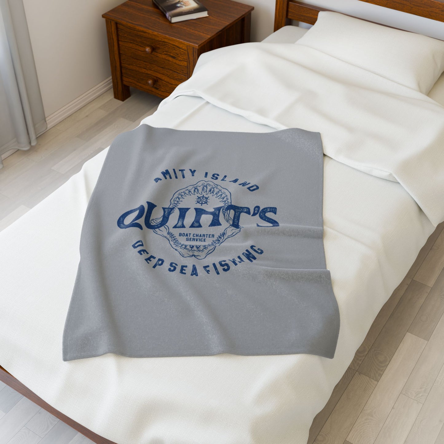 30x40 Gray velveteen plush blanket with vintage blue Quint’s Deep Sea Fishing logo inspired by Jaws, shown on a double bed.
