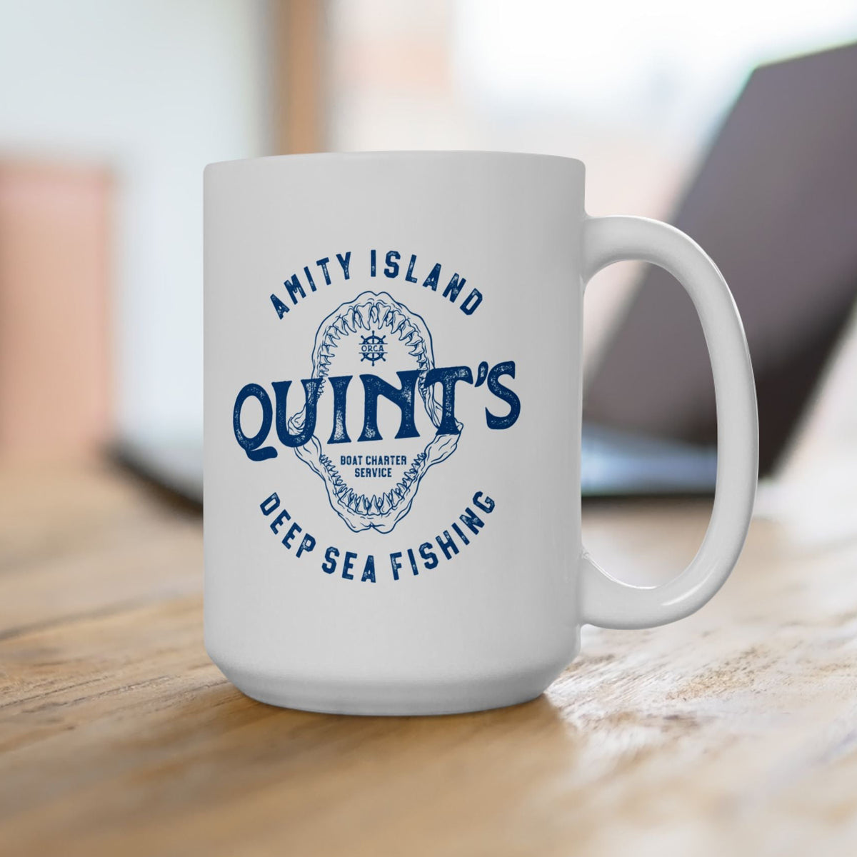 15 oz White mug with blue Amity Island Quint's Deep Sea Fishing boat charter logo and shark jaws, inspired by Jaws, on a desk
