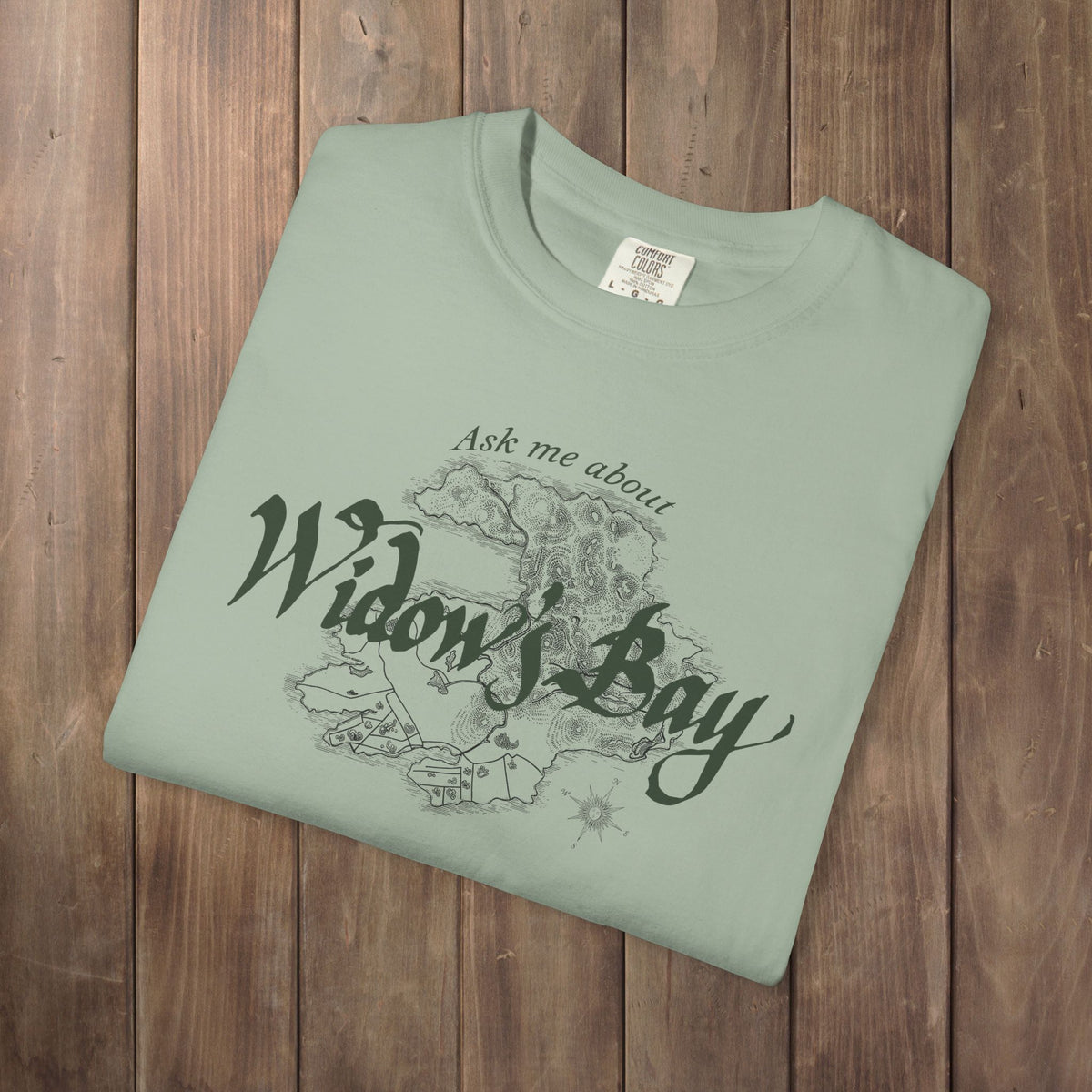 Folded light green Comfort Colors tee with a vintage island map and antique "Ask Me About Widow's Bay" type from the Apple TV show