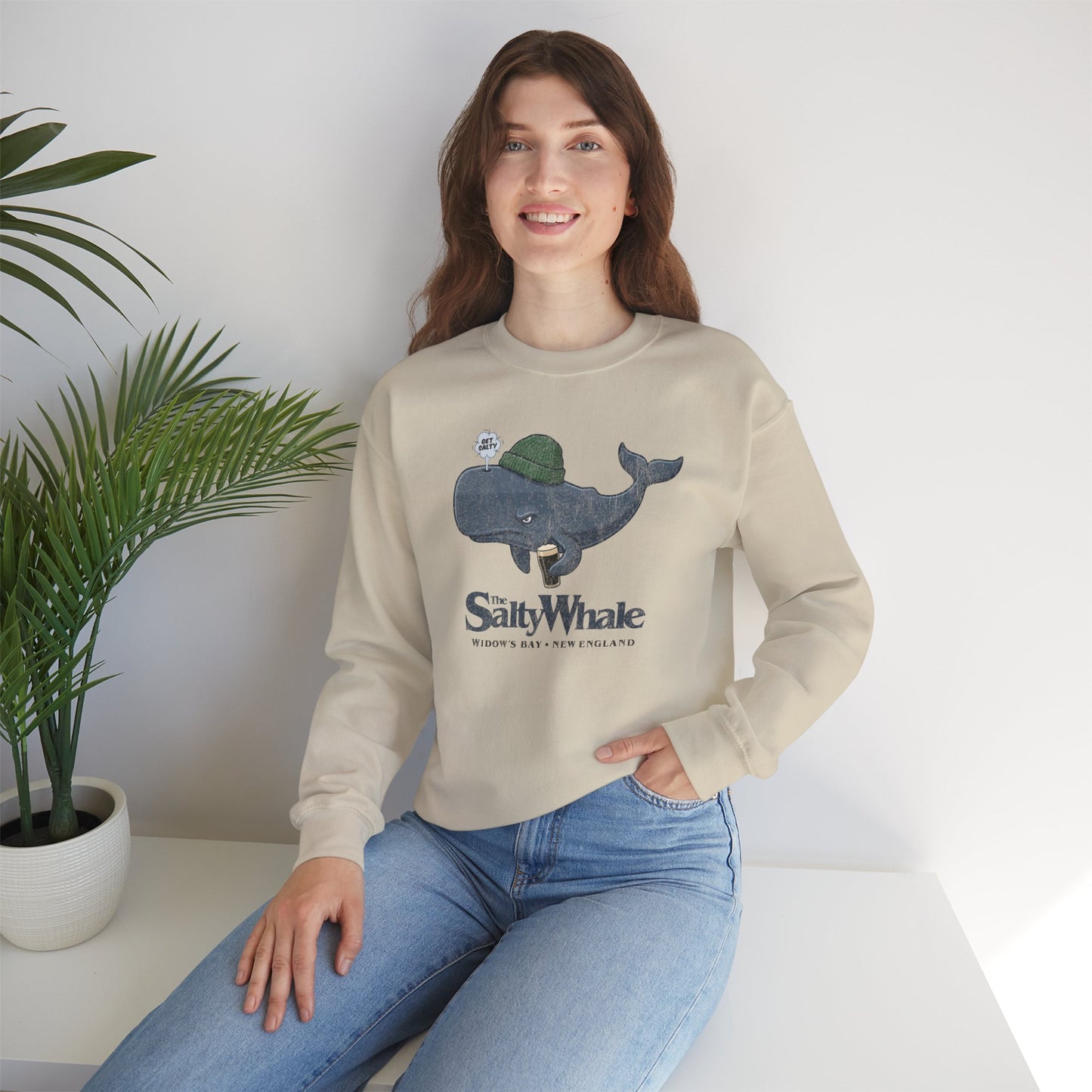 Woman wearing sand colored The Salty Whale cartoon mascot crewneck sweatshirt inspired by Widow's Bay Apple TV series, vintage pub fan pullover