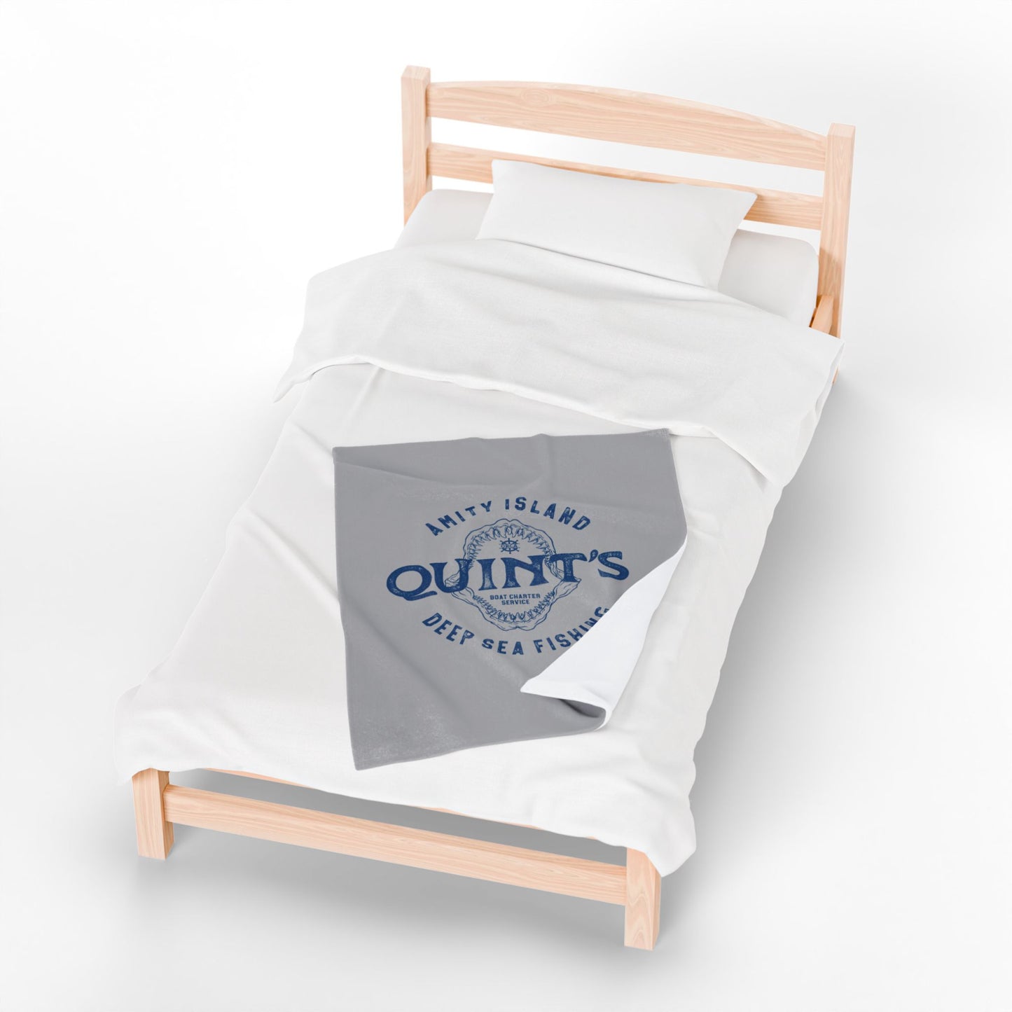 30x40 Gray velveteen plush blanket with vintage blue Quint’s Deep Sea Fishing logo inspired by Jaws, laid on a wood bed.