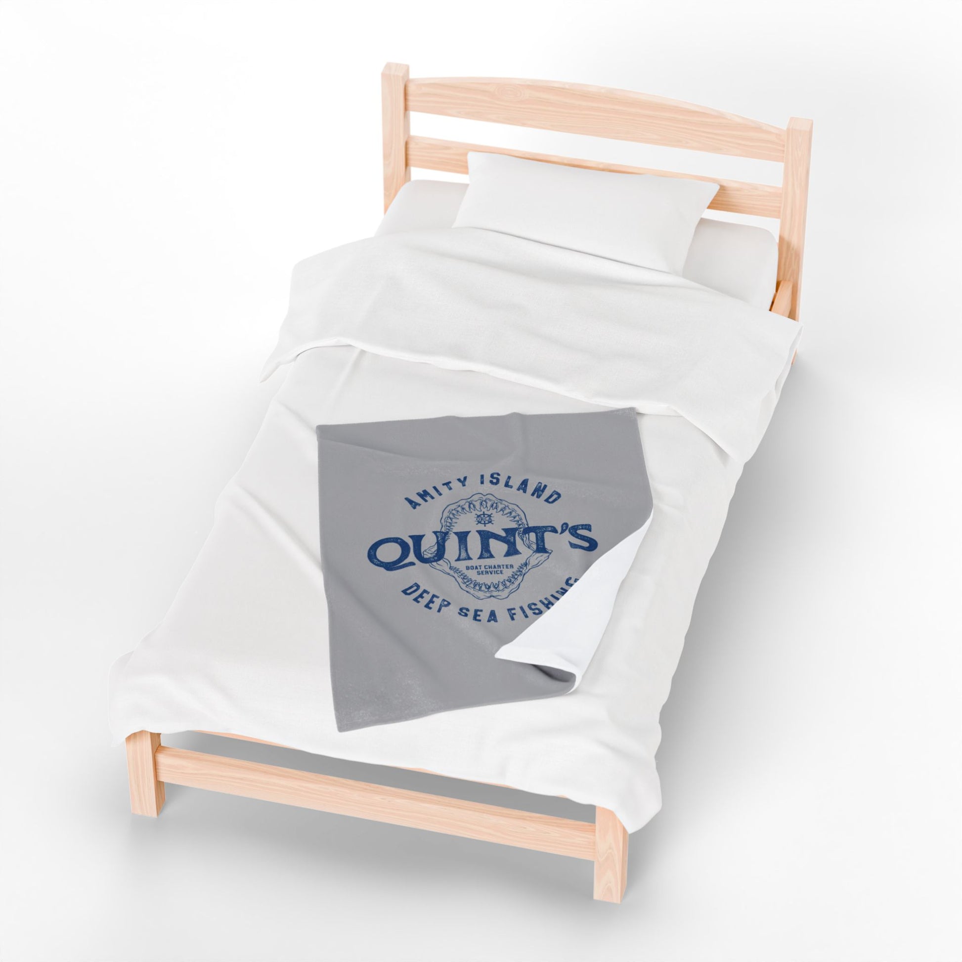 30x40 Gray velveteen plush blanket with vintage blue Quint’s Deep Sea Fishing logo inspired by Jaws, laid on a wood bed.