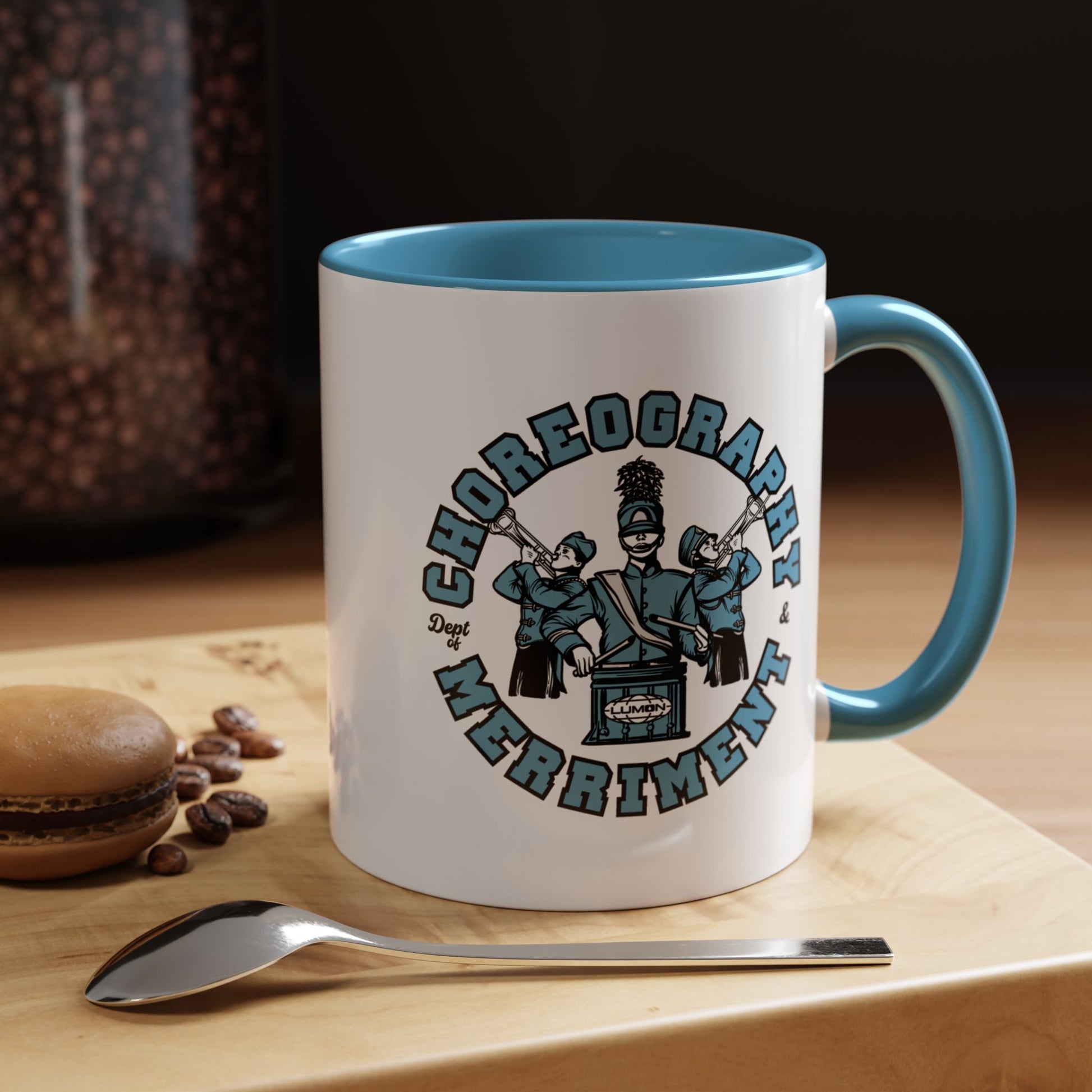 11 oz White ceramic accent mug with blue handle featuring Severance Dept. of Choreography & Merriment graphic, shown on a table.