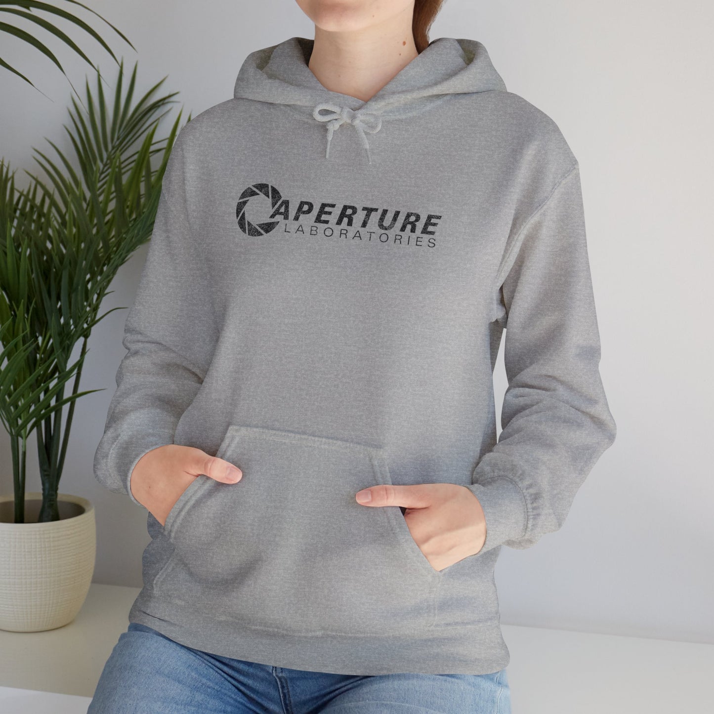 Female model wearing a sport gray heather colored Unisex Hoodie Heavy Blend Hooded Sweatshirt featuring the Aperture Laboratories logo from the video game Portal and Portal 2 in a vintage distressed style, sold by ScriptedBrand.