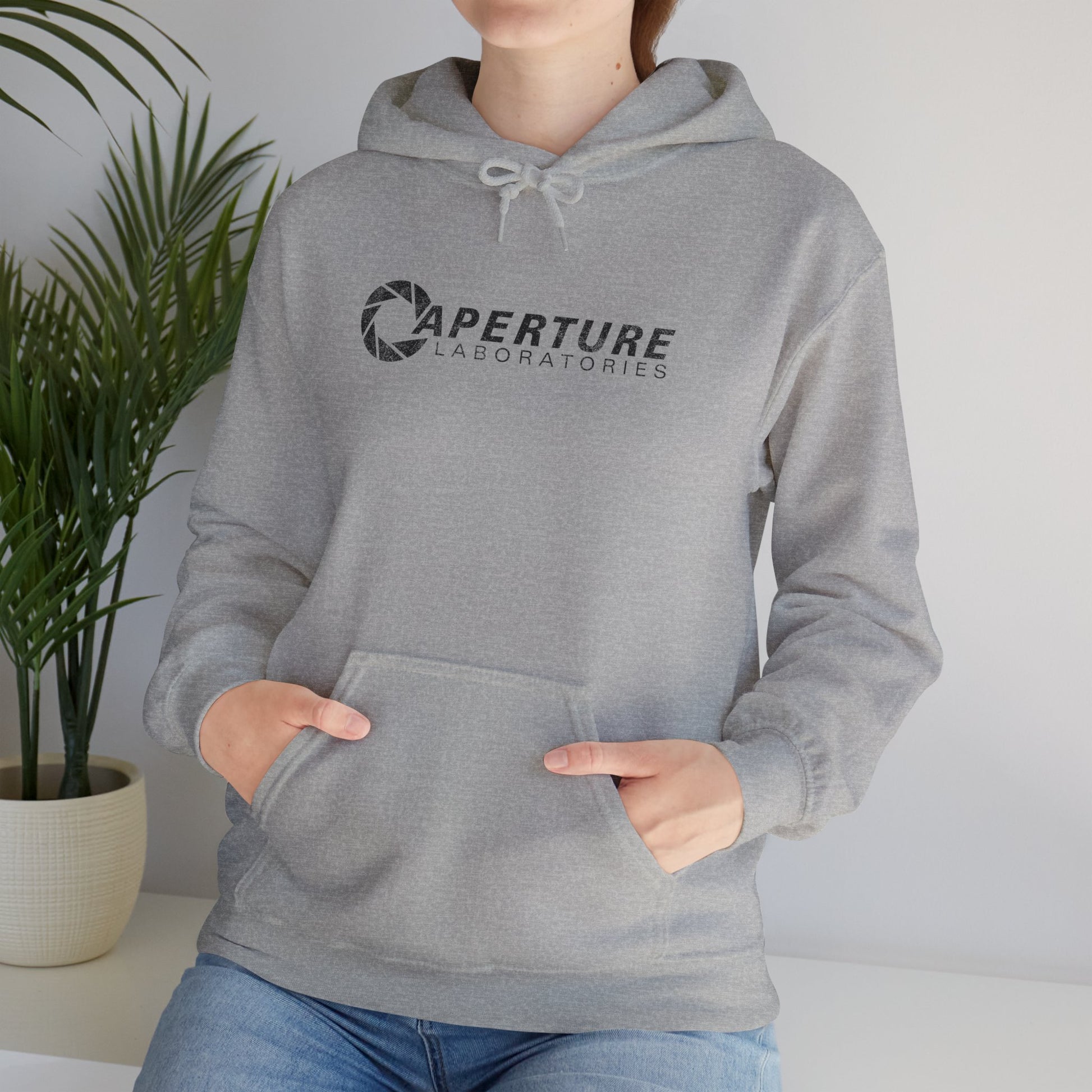 Female model wearing a sport gray heather colored Unisex Hoodie Heavy Blend Hooded Sweatshirt featuring the Aperture Laboratories logo from the video game Portal and Portal 2 in a vintage distressed style, sold by ScriptedBrand.