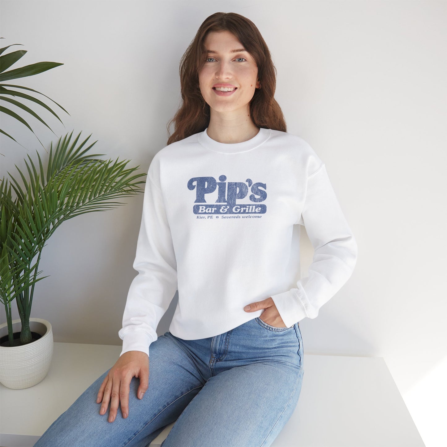 Female model wearing a white soft Gildan 18000 sweatshirt featuring the Pips Bar and Grill logo Severeds Welcome from the TV show Severance in a vintage distressed ink-stamped worn-in style.