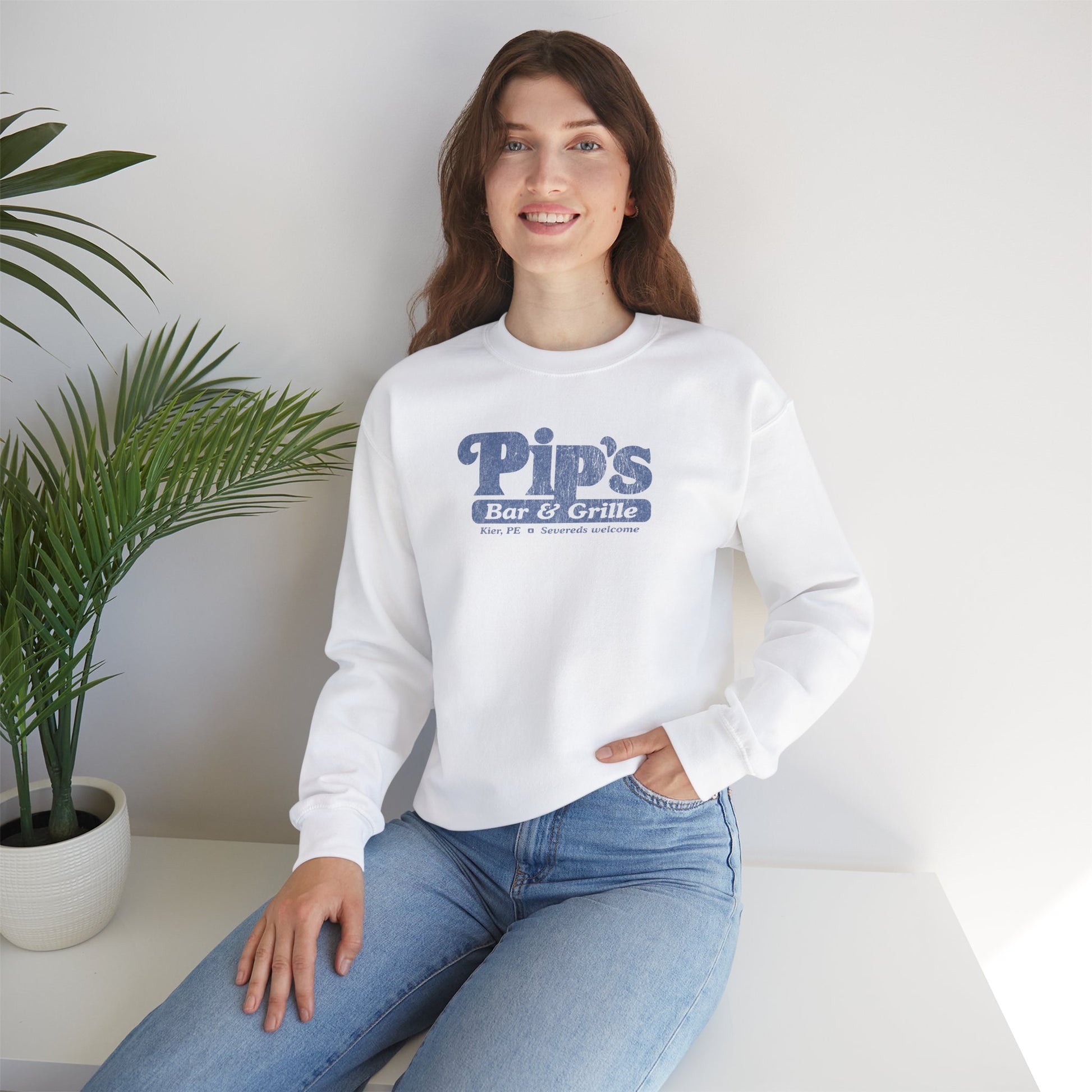 Female model wearing a white soft Gildan 18000 sweatshirt featuring the Pips Bar and Grill logo Severeds Welcome from the TV show Severance in a vintage distressed ink-stamped worn-in style.
