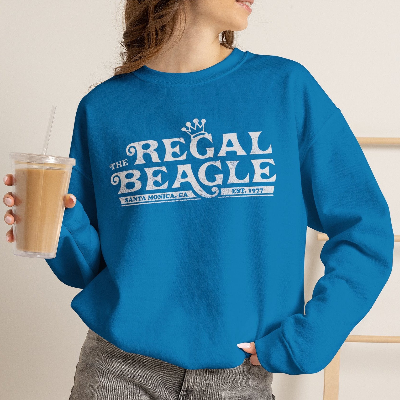 Person wearing Saphire blue crewneck sweatshirt with vintage distressed blue Regal Beagle Three's Company logo