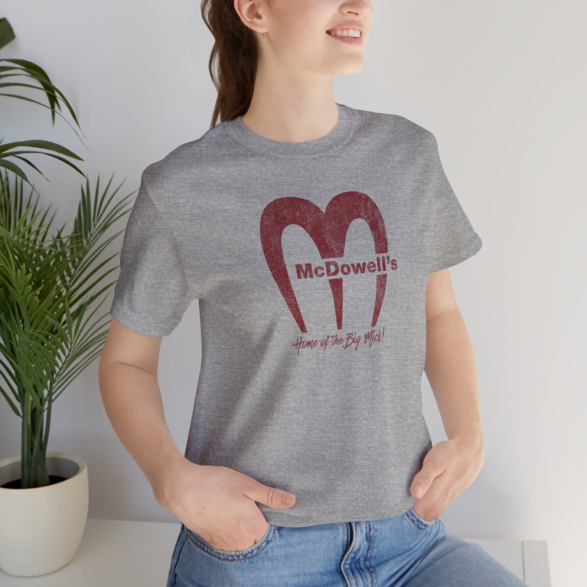 Woman wearing heather gray Bella+Canvas t-shirt featuring the McDowells logo from the movie Coming to America in a vintage distressed style.