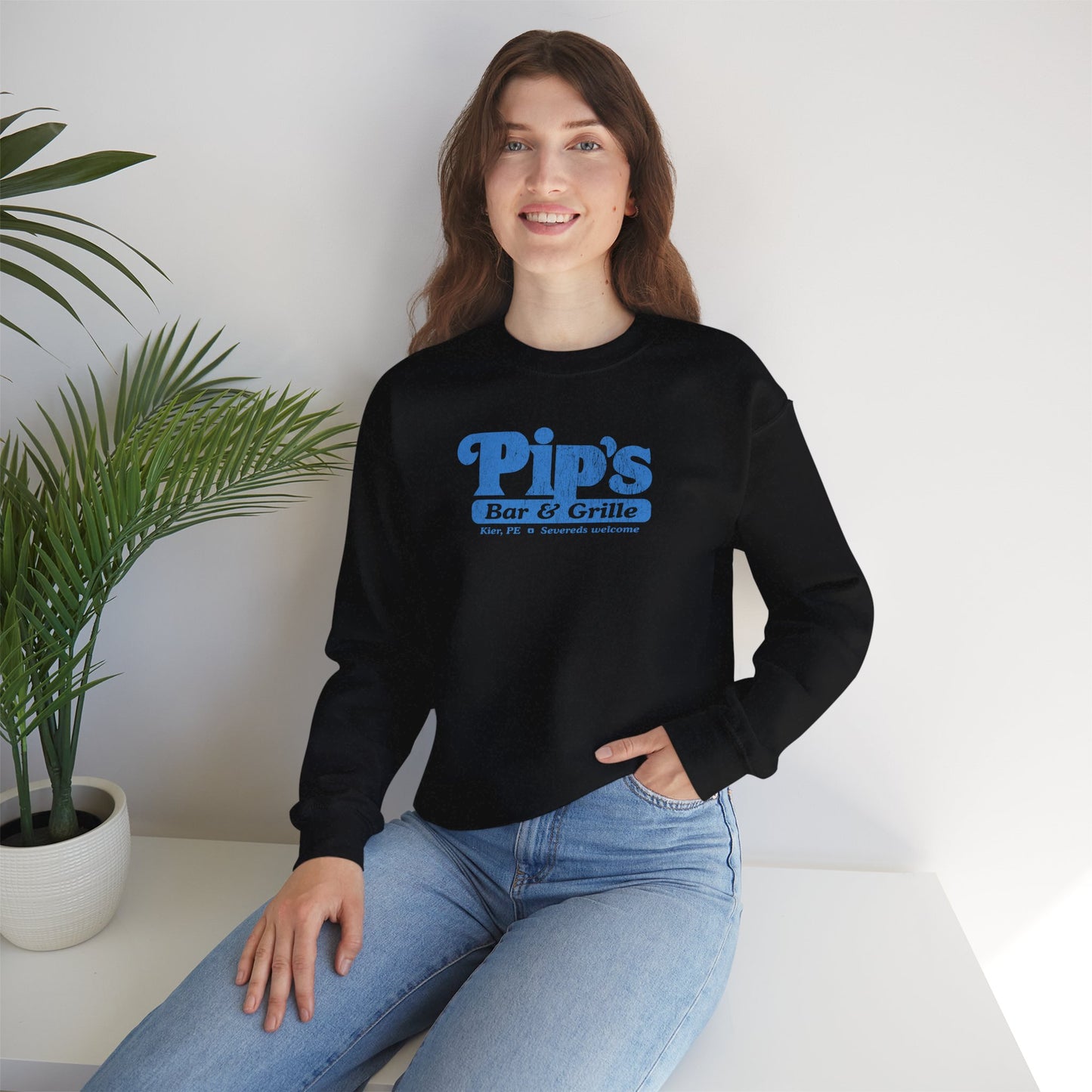 Female model wearing a black soft Gildan 18000 sweatshirt featuring the Pips Bar and Grill logo Severeds Welcome from the TV show Severance in a vintage distressed ink-stamped worn-in style.