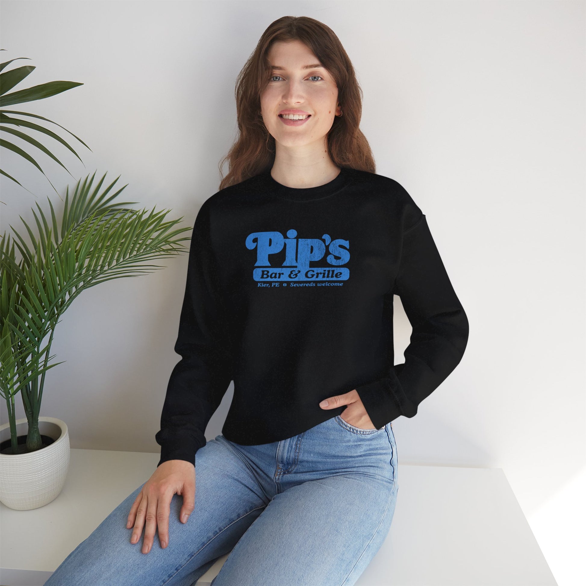 Female model wearing a black soft Gildan 18000 sweatshirt featuring the Pips Bar and Grill logo Severeds Welcome from the TV show Severance in a vintage distressed ink-stamped worn-in style.