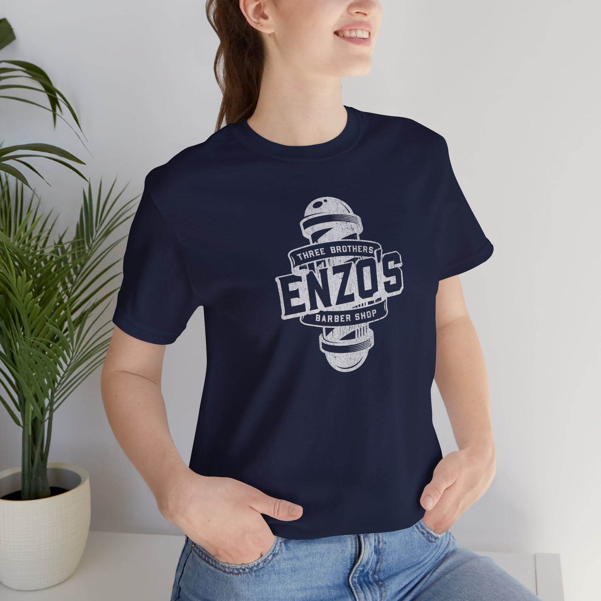 Woman wearing a navy blue t-shirt with the Enzo's Barber Shop logo graphic inspired by the TV show Seinfeld in a vintage distressed style.