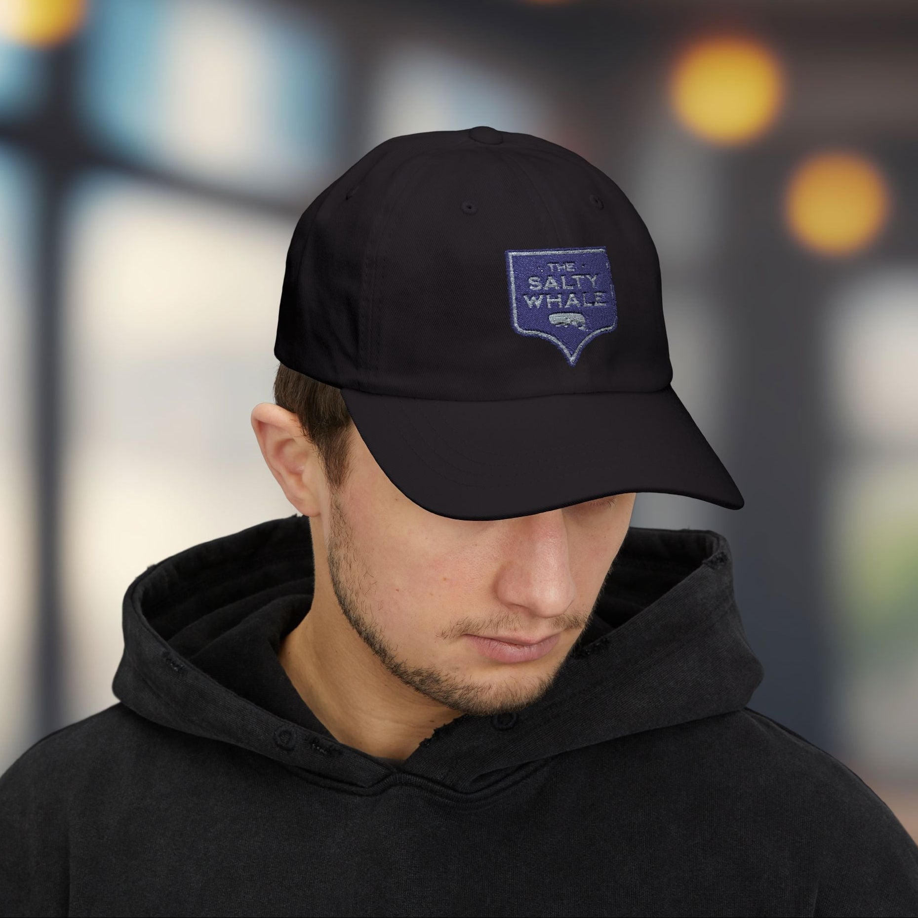 Man wearing black 'The Salty Whale' embroidered sign logo dad cap inspired by Widow's Bay Apple TV series, 100% cotton baseball hat