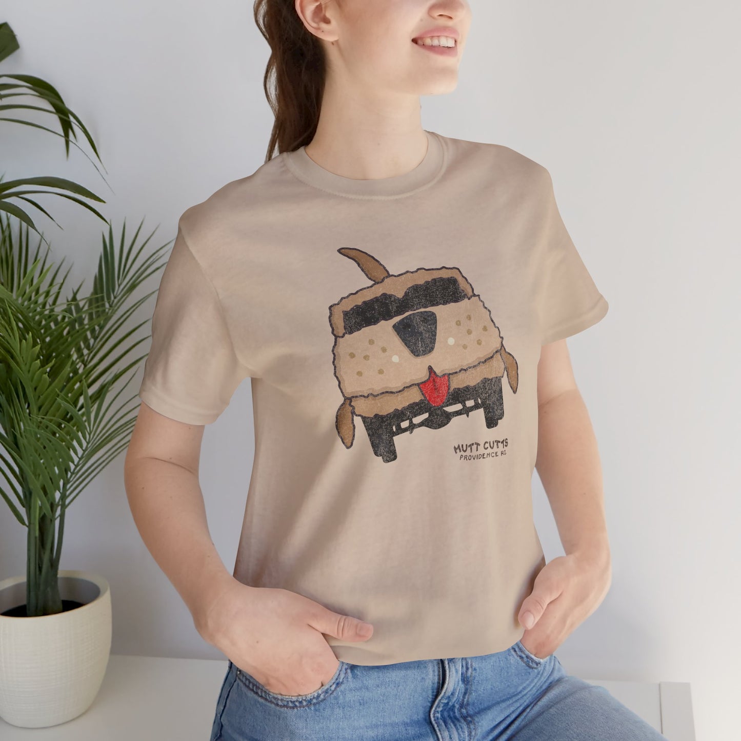 Woman wearing tan Bella+Canvas tee with vintage Mutt Cutts dog van graphic inspired by Dumb and Dumber movie.
