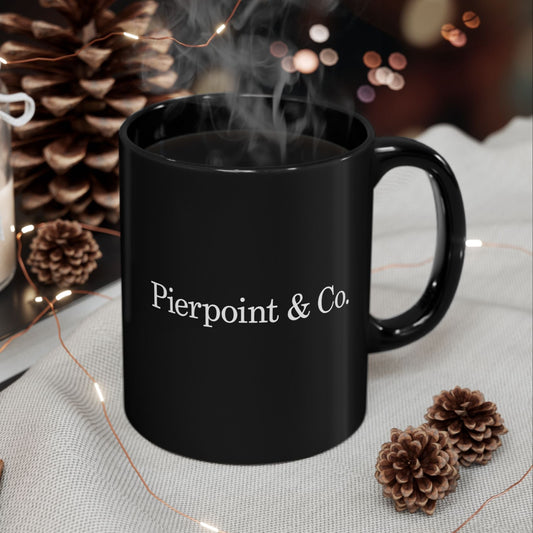 Black mug with 'Pierpoint & Co.' text, steaming hot beverage, pinecones, and lights on a textured surface.