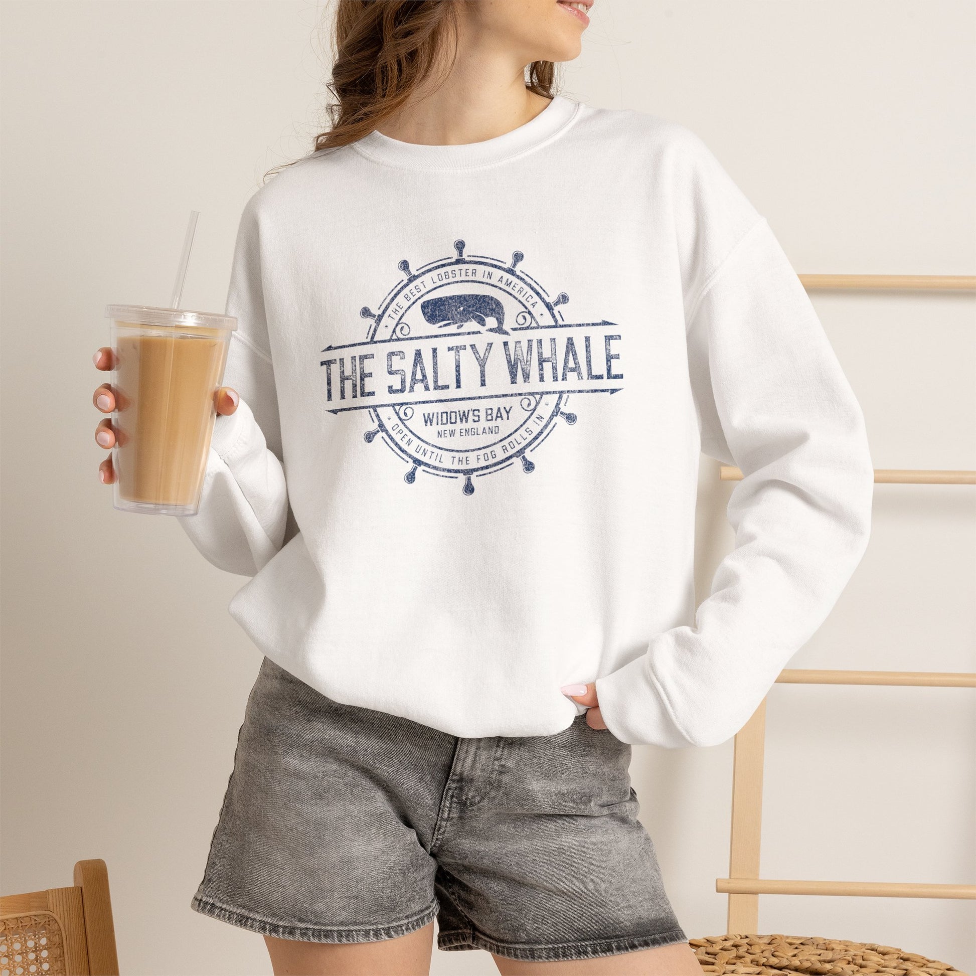 Woman wearing white Gildan crewneck sweatshirt with the distressed Salty Whale maritime crest logo from TV show Widow's Bay