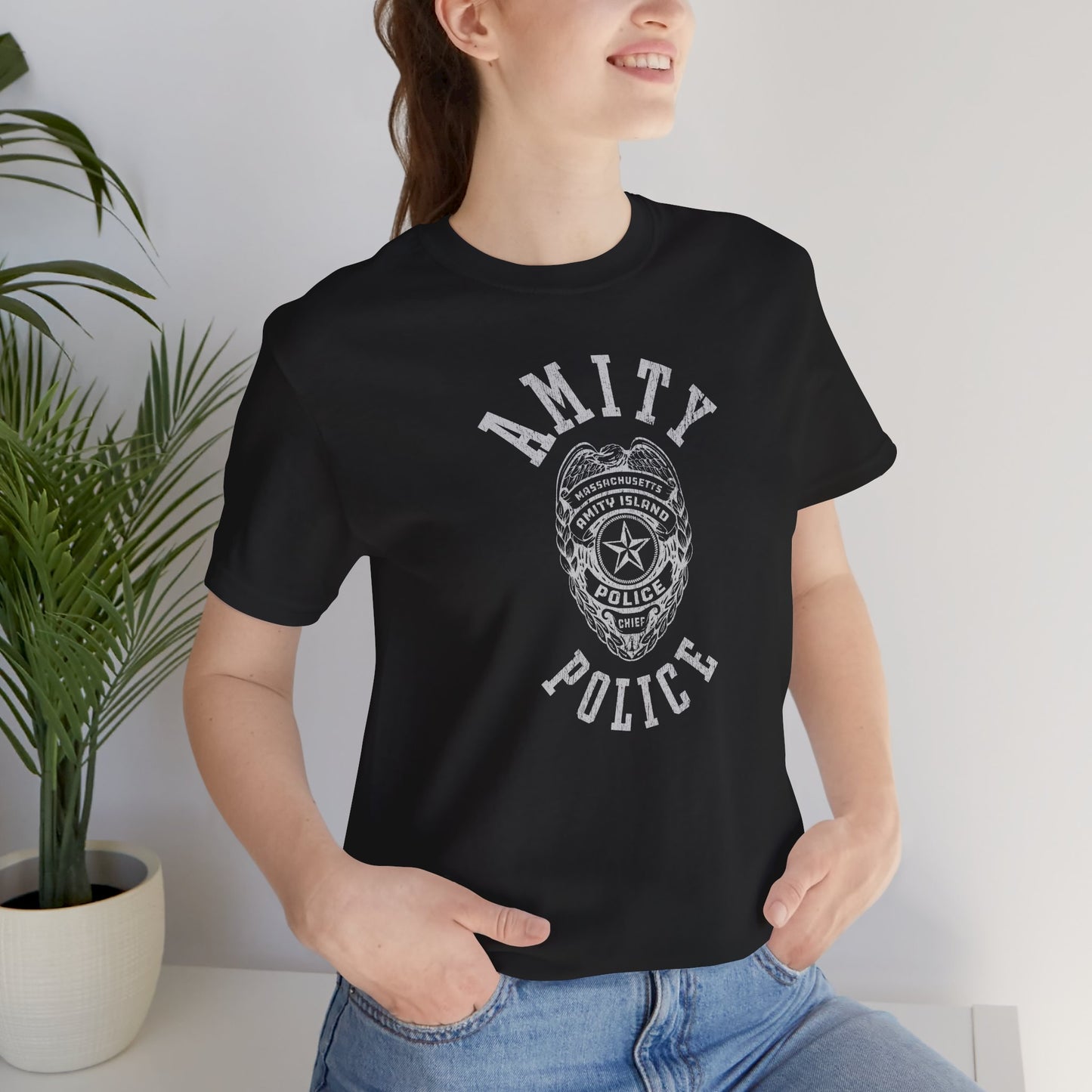 Female model wearing a black colored Soft unisex Bella+Canvas 3001 short-sleeve t-shirt featuring an Amity Island Police logo graphic, designed by ScriptedBrand, and  inspired by the movie Jaws in a vintage distressed style.