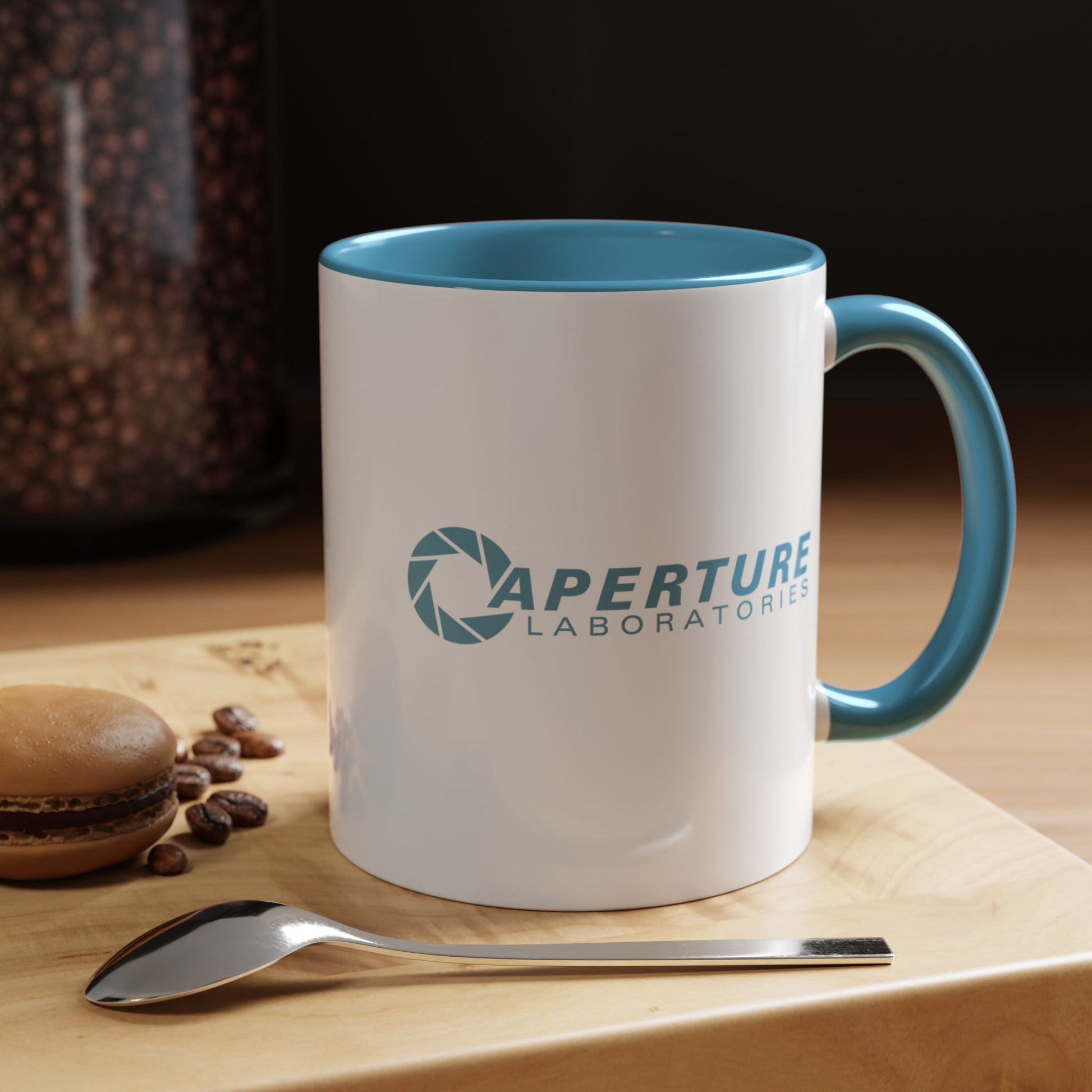White mug with blue interior and handle featuring 'Aperture Laboratories' logo, placed on a wooden surface with coffee beans and a spoon.