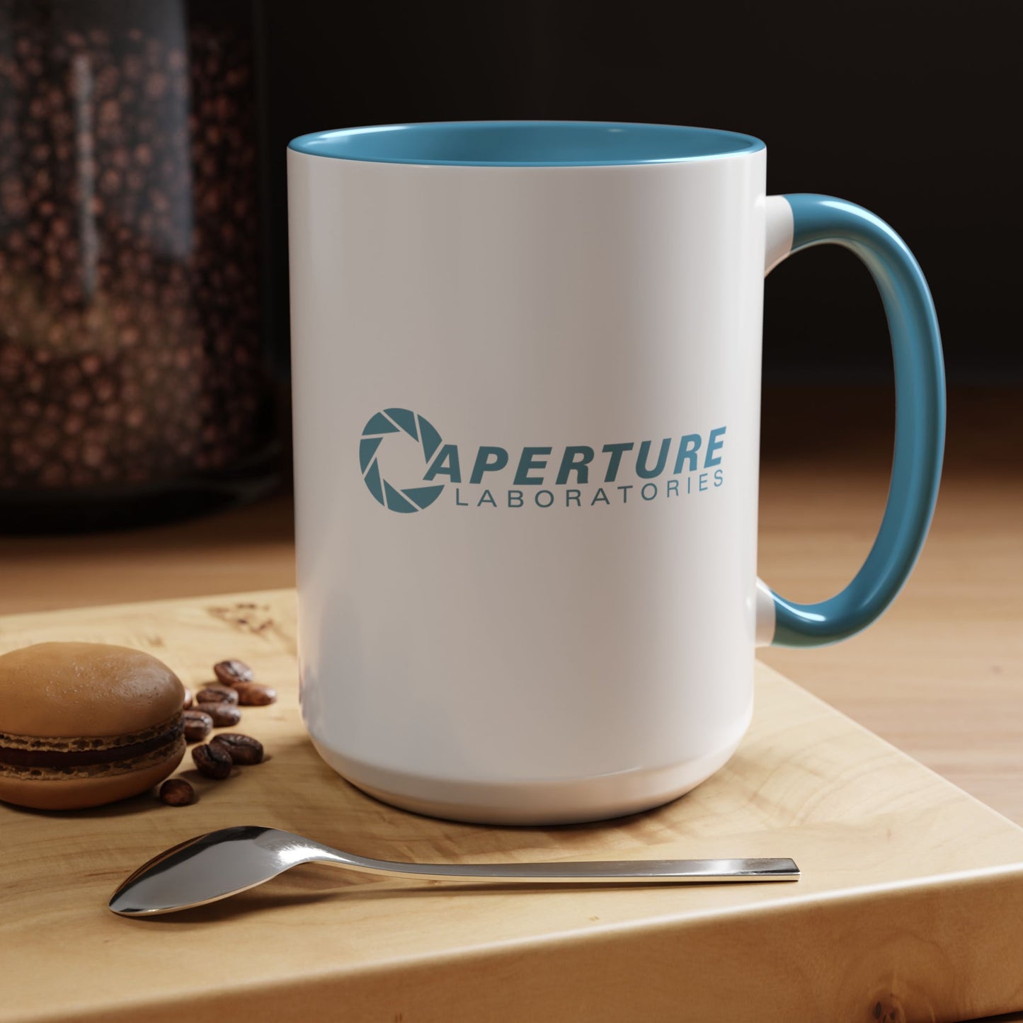 Mug with 'Aperture Laboratories' logo on a wooden surface with coffee beans and a macaron.