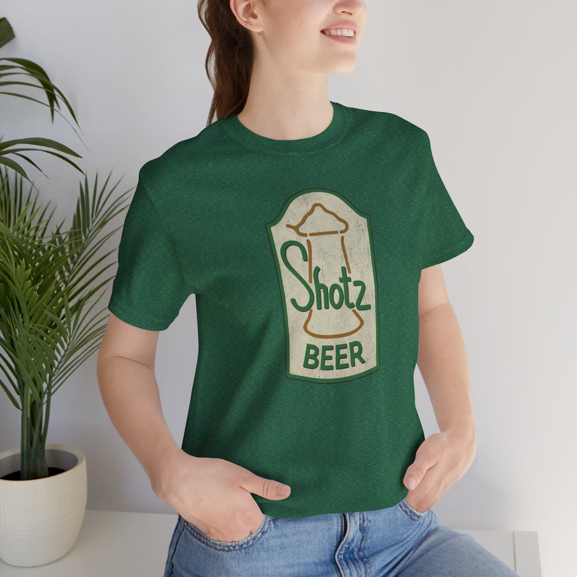 Model wearing heather grass green t-shirt with vintage Shotz Beer Brewery logo graphic, inspired by TV show Laverne & Shirley.
