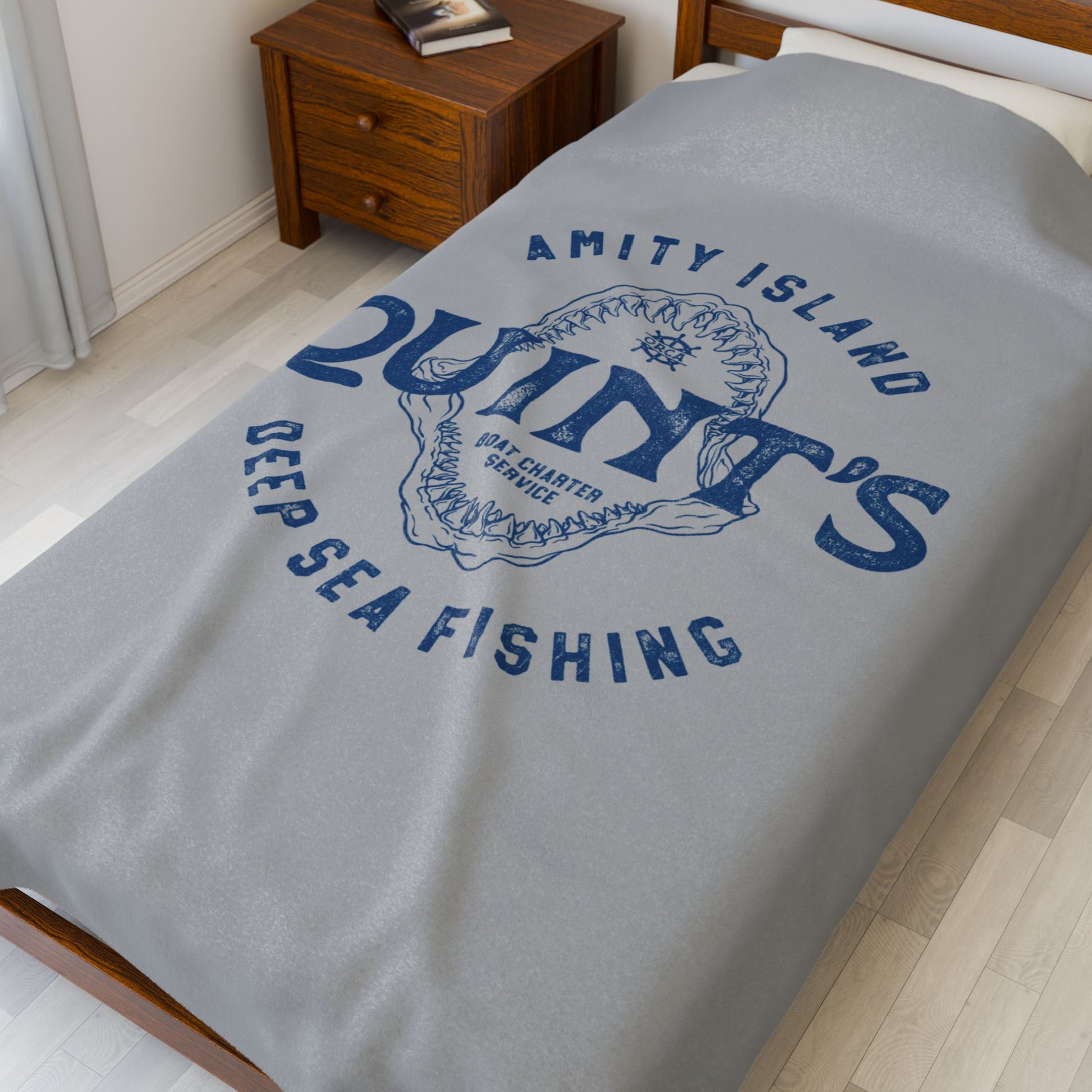 60x80 large Gray velveteen plush blanket with vintage blue Quint’s Deep Sea Fishing logo inspired by Jaws, shown on a double bed.