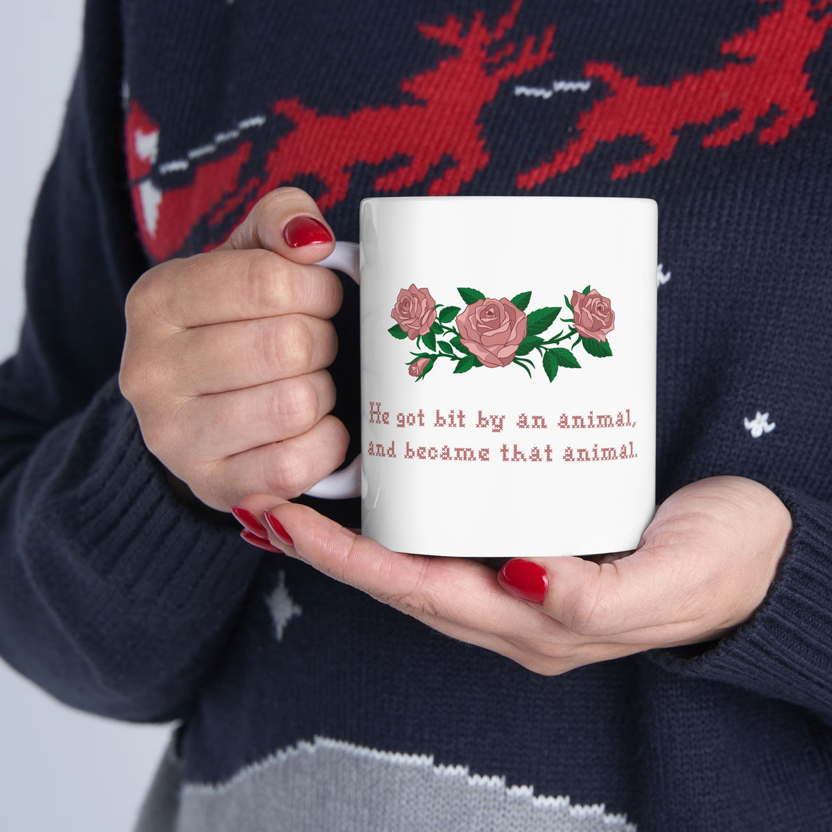 Woman holding a white ceramic mug with a printed design of pink roses and green leaves, featuring the text 'He got bit by an animal, and became that animal' in cross stitch style, inspired by Ruth on Widows Bay.