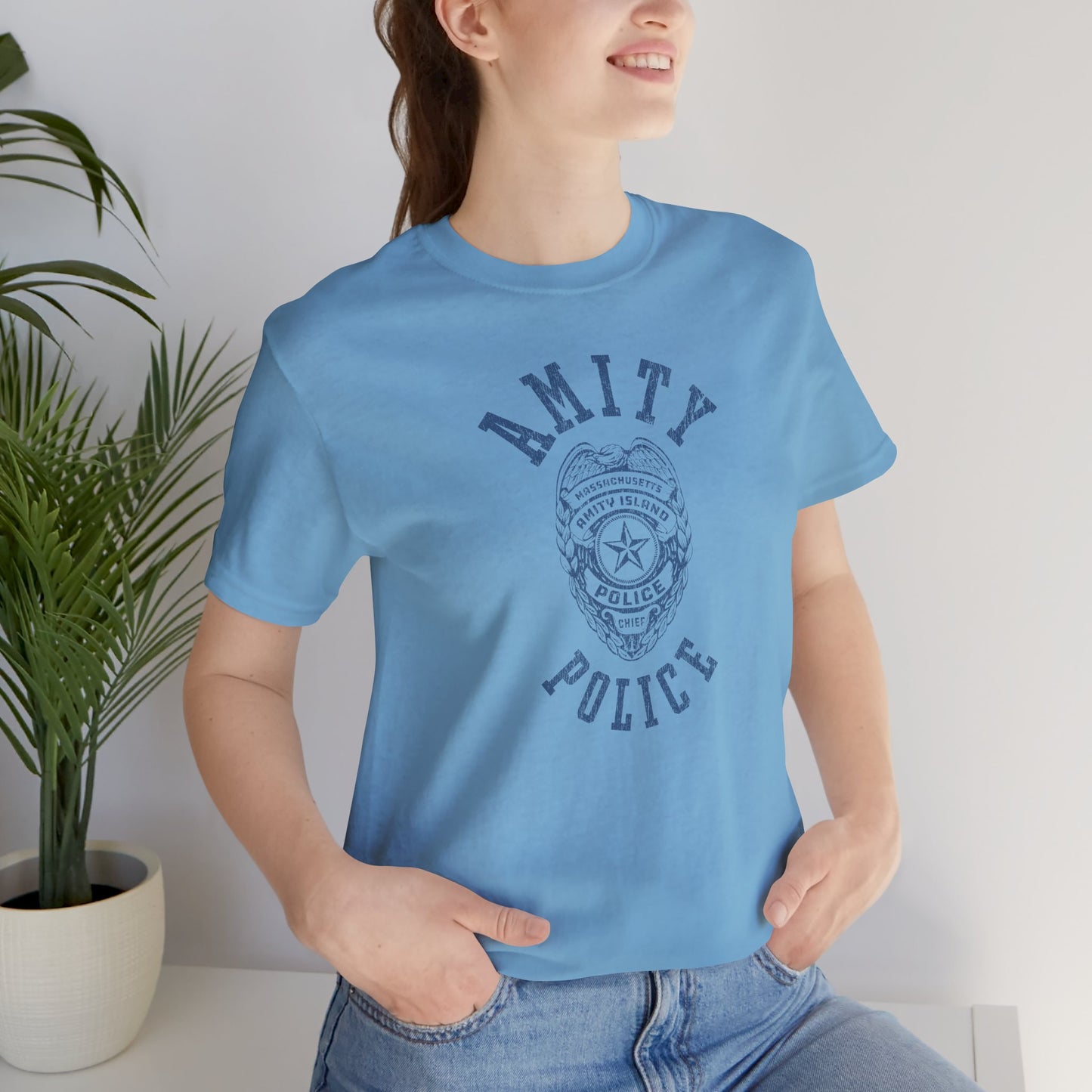 Female model wearing an ocean blue colored Soft unisex Bella+Canvas 3001 short-sleeve t-shirt featuring an Amity Island Police logo graphic, designed by ScriptedBrand, and  inspired by the movie Jaws in a vintage distressed style.