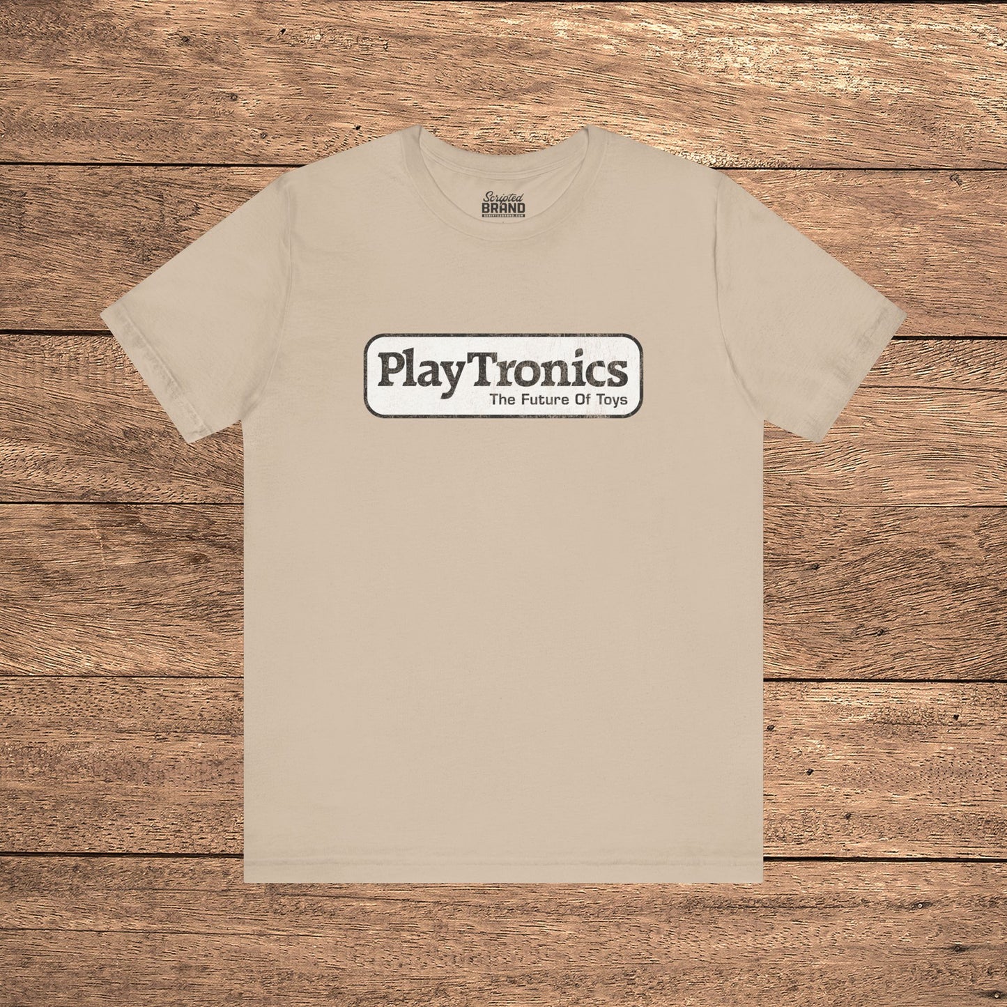 Tan PlayTronics Sneakers movie logo t-shirt on Bella+Canvas 3001, vintage distressed print, shown on wood floor.
