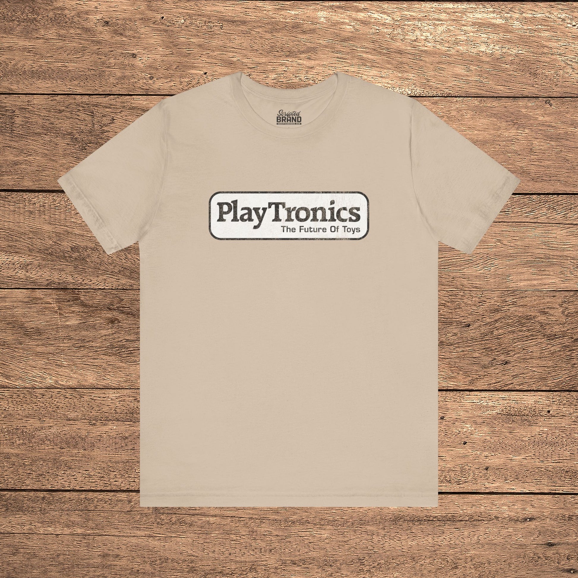 Tan PlayTronics Sneakers movie logo t-shirt on Bella+Canvas 3001, vintage distressed print, shown on wood floor.