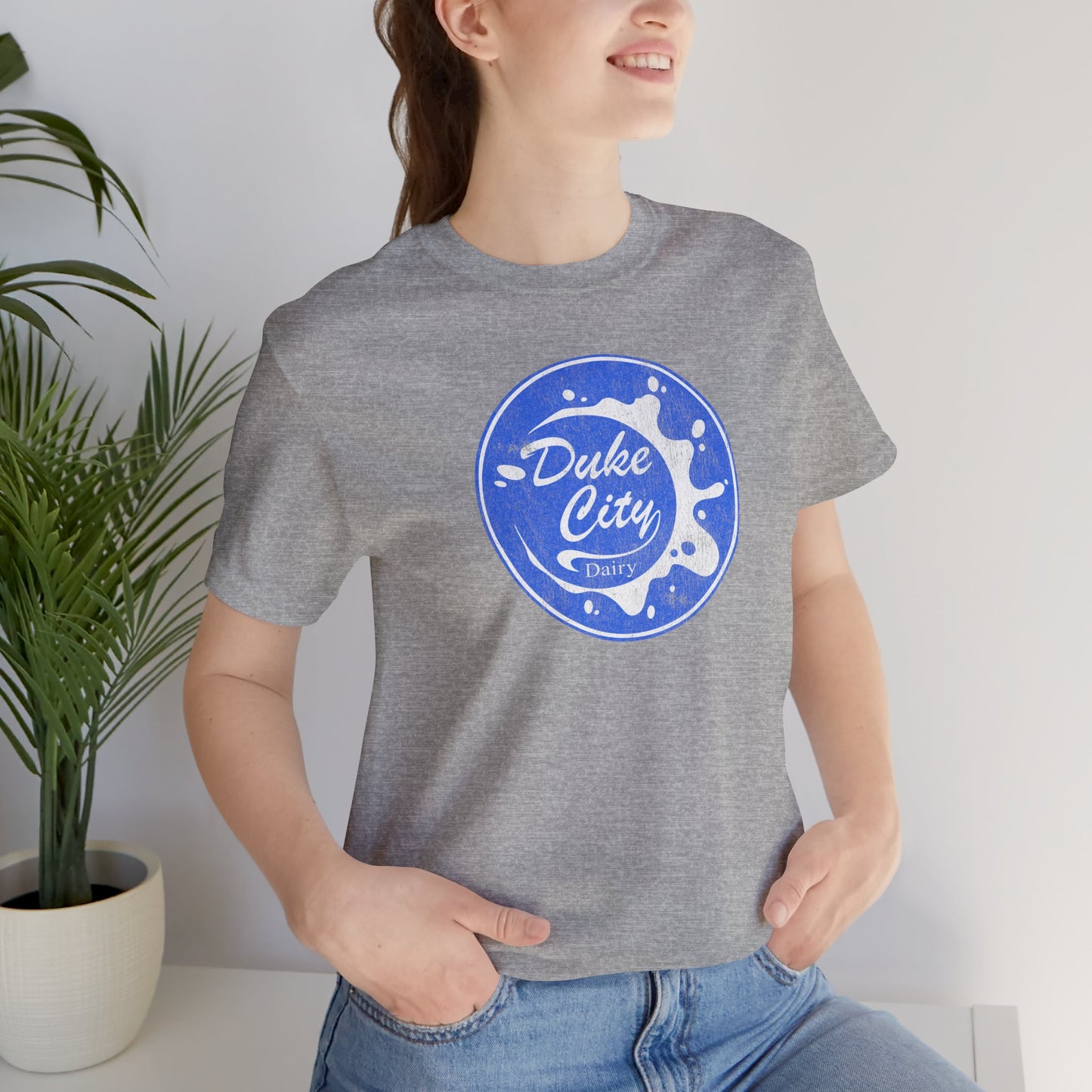 Woman wearing heather gray t-shirt with vintage distressed Duke City Dairy logo inspired by TV Show Pluribus.