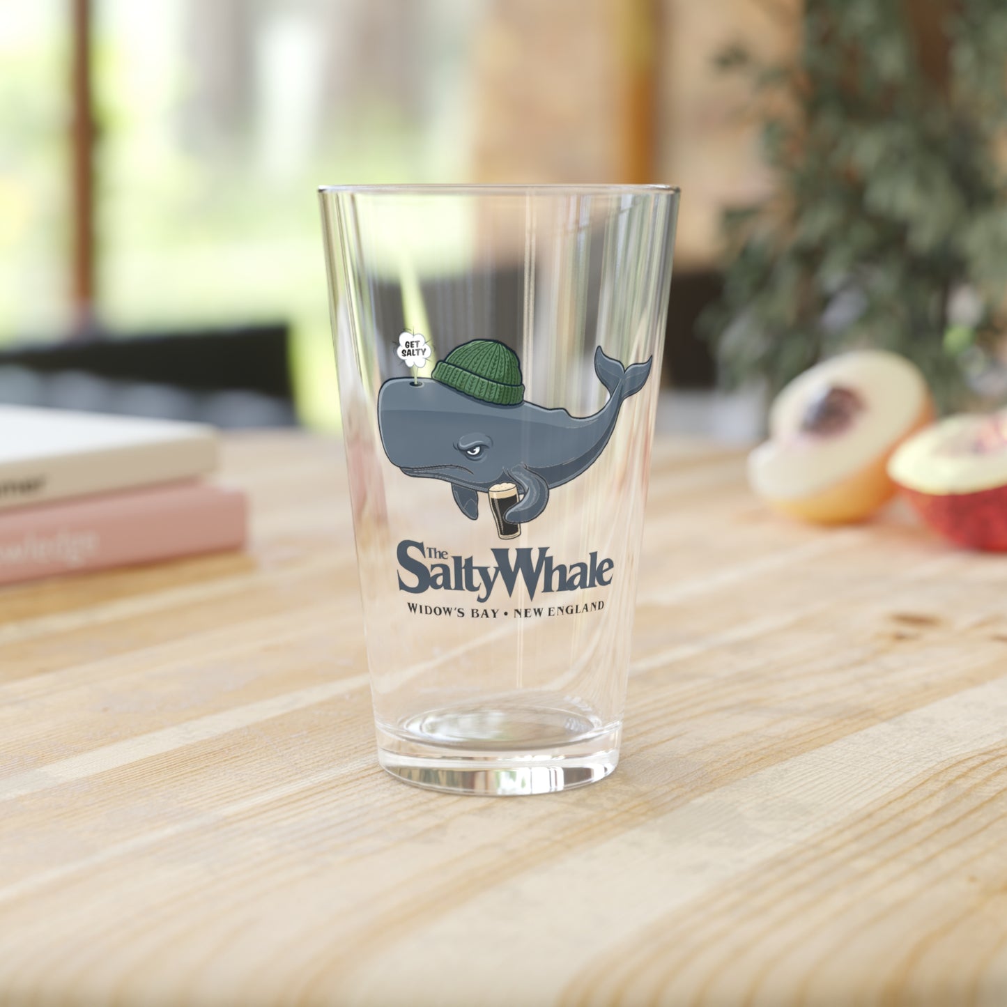 The Salty Whale cartoon mascot pint glass inspired by Widow's Bay Apple TV series, 16oz beer glass in a kitchen