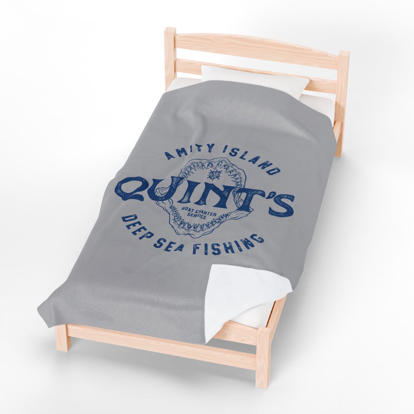 60x80 large Gray velveteen plush blanket with vintage blue Quint’s Deep Sea Fishing logo inspired by Jaws, laid on a wood bed.