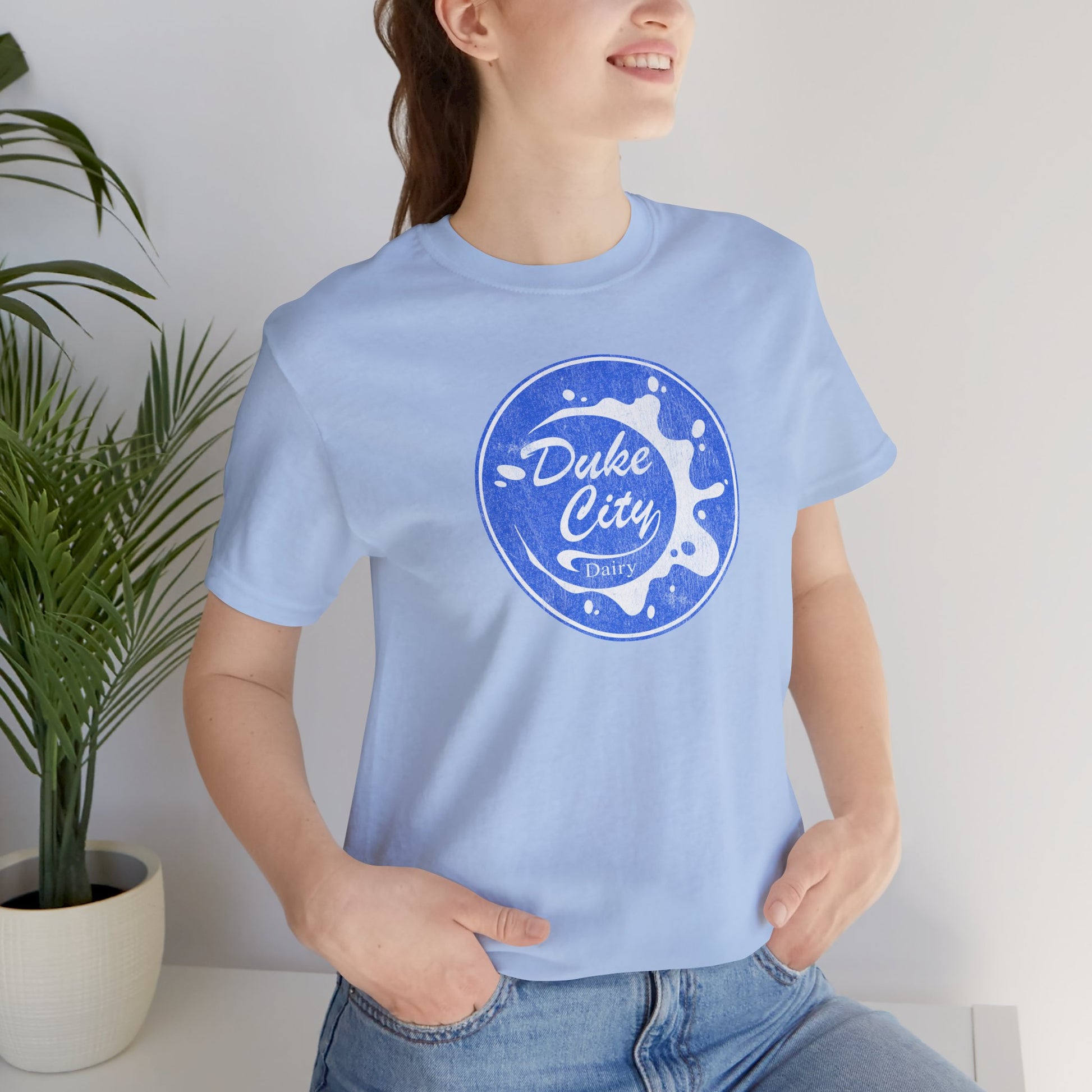Woman wearing light blue t-shirt with vintage distressed Duke City Dairy logo inspired by TV Show Pluribus.