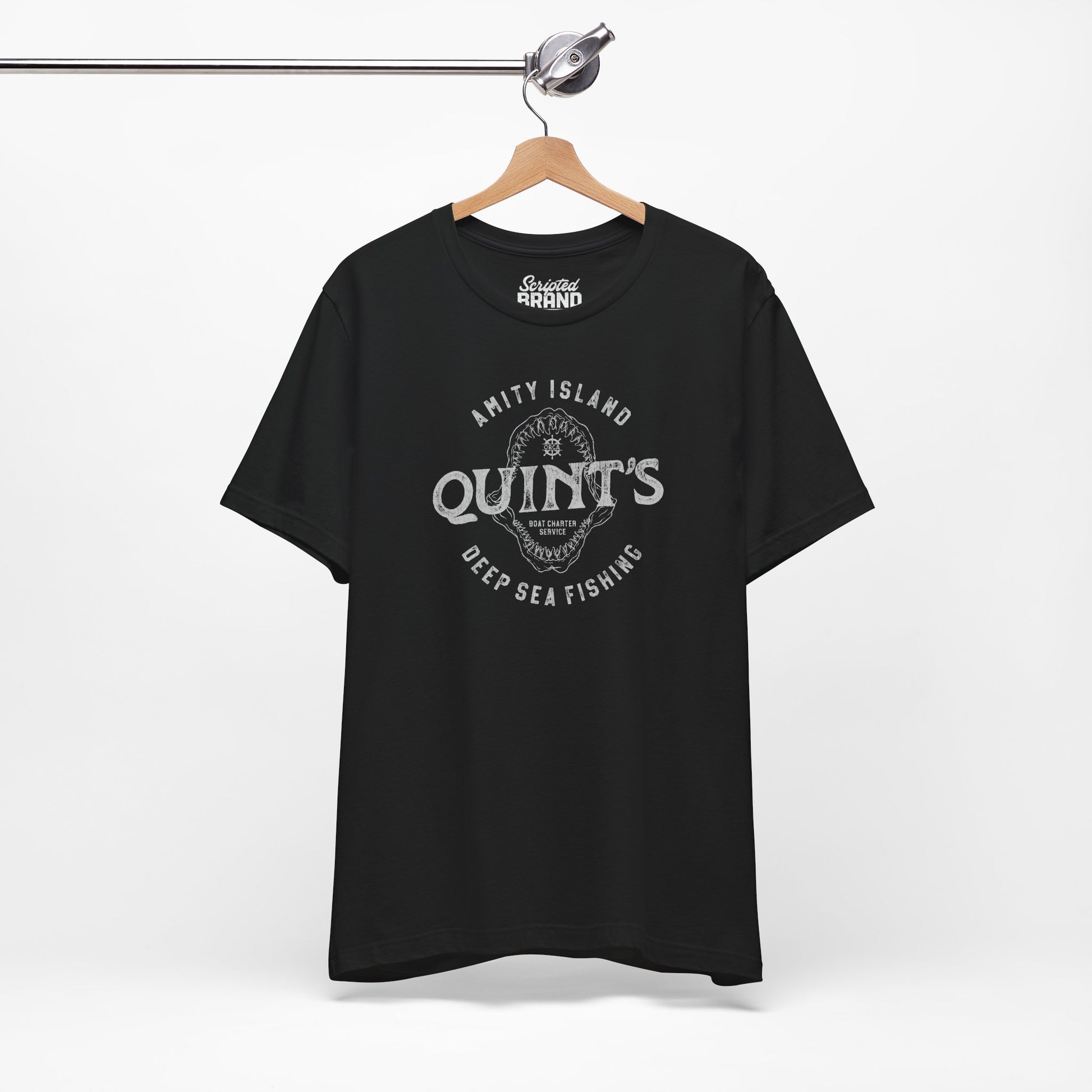 Black colored Soft short-sleeve t-shirt on a hanger featuring the Quint's Deep Sea Fishing Boat Charters logo graphic inspired by the movie Jaws in a vintage distressed ink-stamped worn-in style.