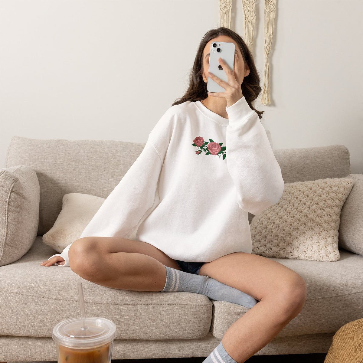 Person wearing a white crewneck sweatshirt with three pink roses and green leaves printed across the chest, inspired by Ruth of Widow's Bay.