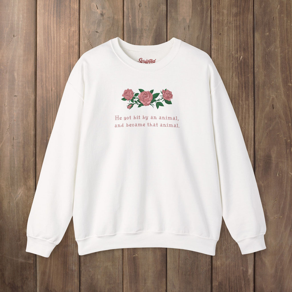 A white crewneck sweatshirt with a graphic of pink roses and green leaves on the chest, accompanied by the text 'He got hit by an animal, and became that animal.' in pink.