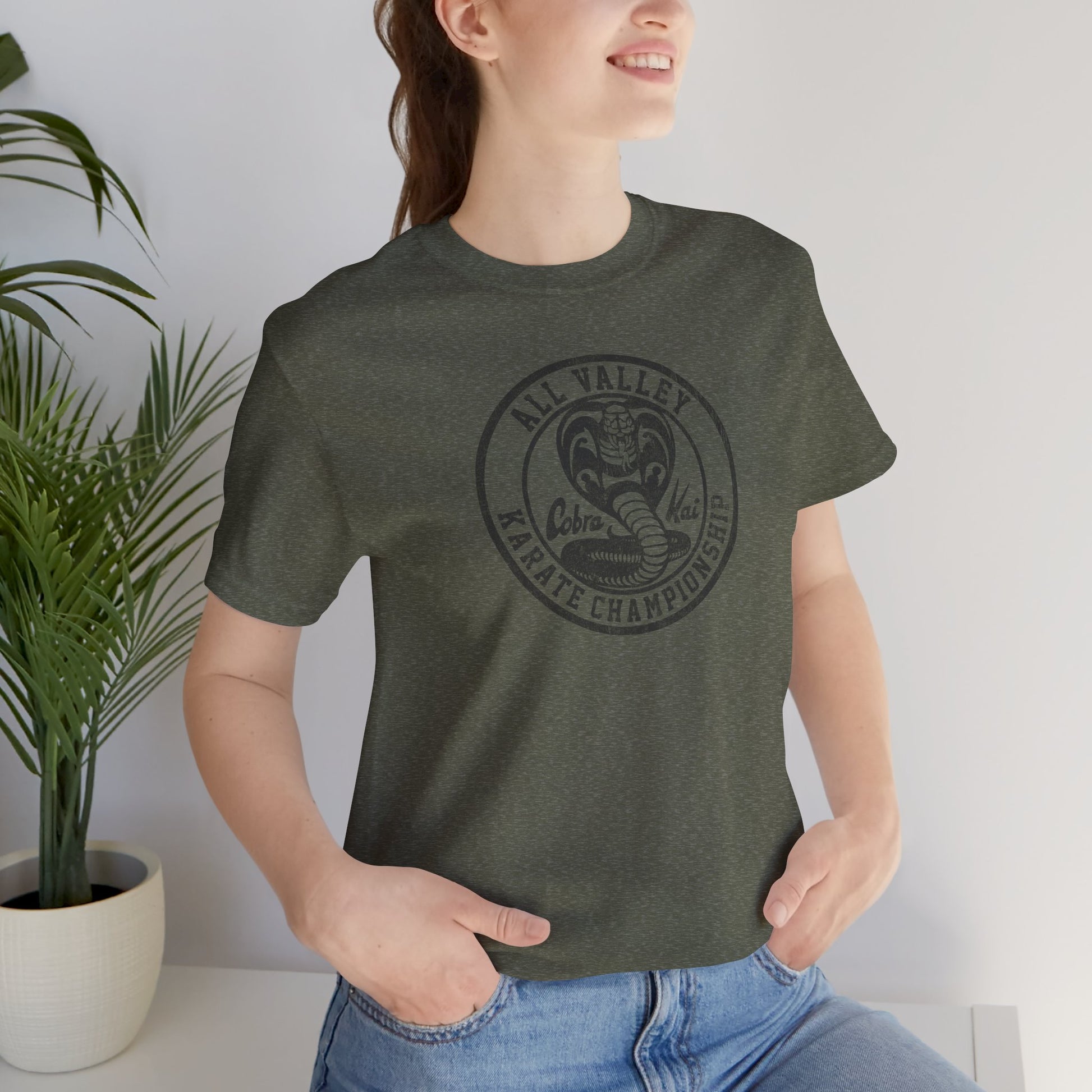 Woman wearing heather military green Cobra Kai All Valley Karate Championship vintage distressed graphic t-shirt, soft Bella+Canvas cotton Karate Kid tee