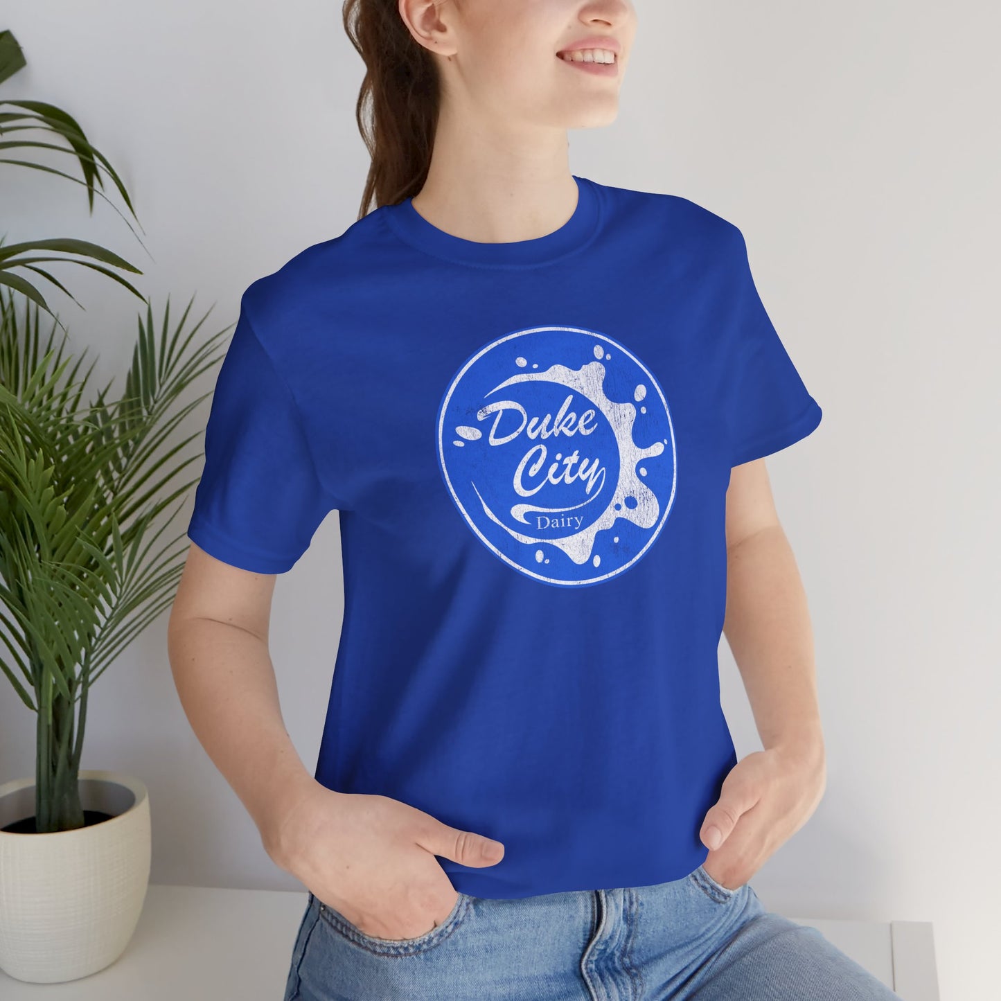 Woman wearing royal blue t-shirt with vintage distressed Duke City Dairy logo inspired by TV Show Pluribus.