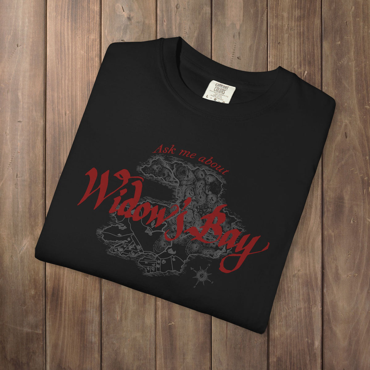 Folded black Comfort Colors tee with a vintage island map and antique "Ask Me About Widow's Bay" type from the Apple TV show